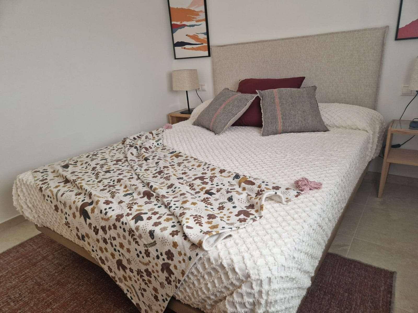 Nahaufnahme eines Doppelbettes in einem hellen Schlafzimmer mit beigem Kopfteil und dekorativen Kissen.