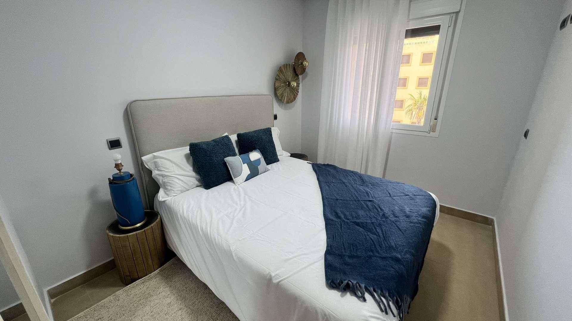 Schlafzimmer mit Doppelbett, blauen Akzenten und einem Fenster für natürliches Licht.