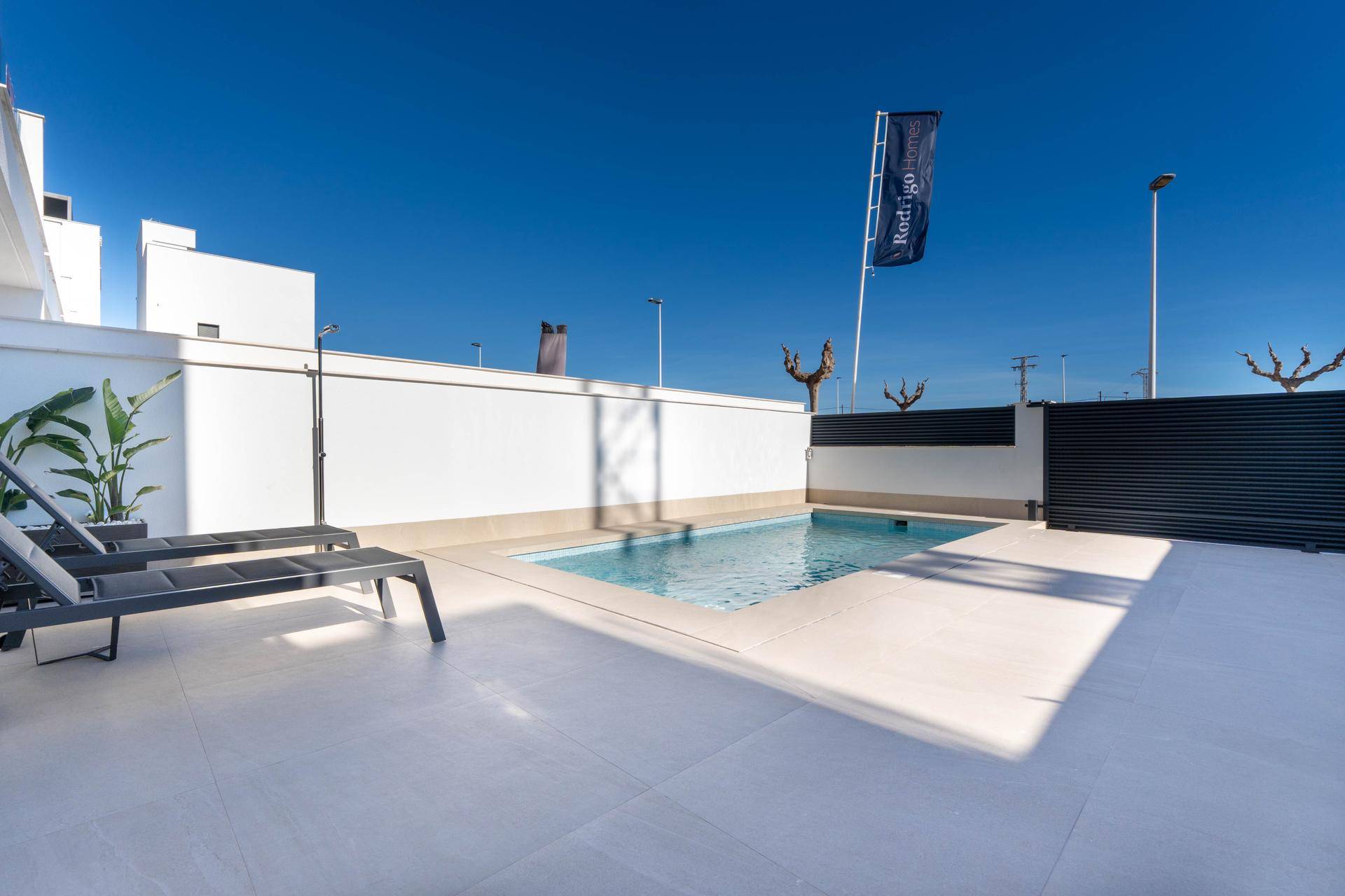 Sonniger Terrassenbereich mit privatem Pool und Liegestühlen unter blauem Himmel.