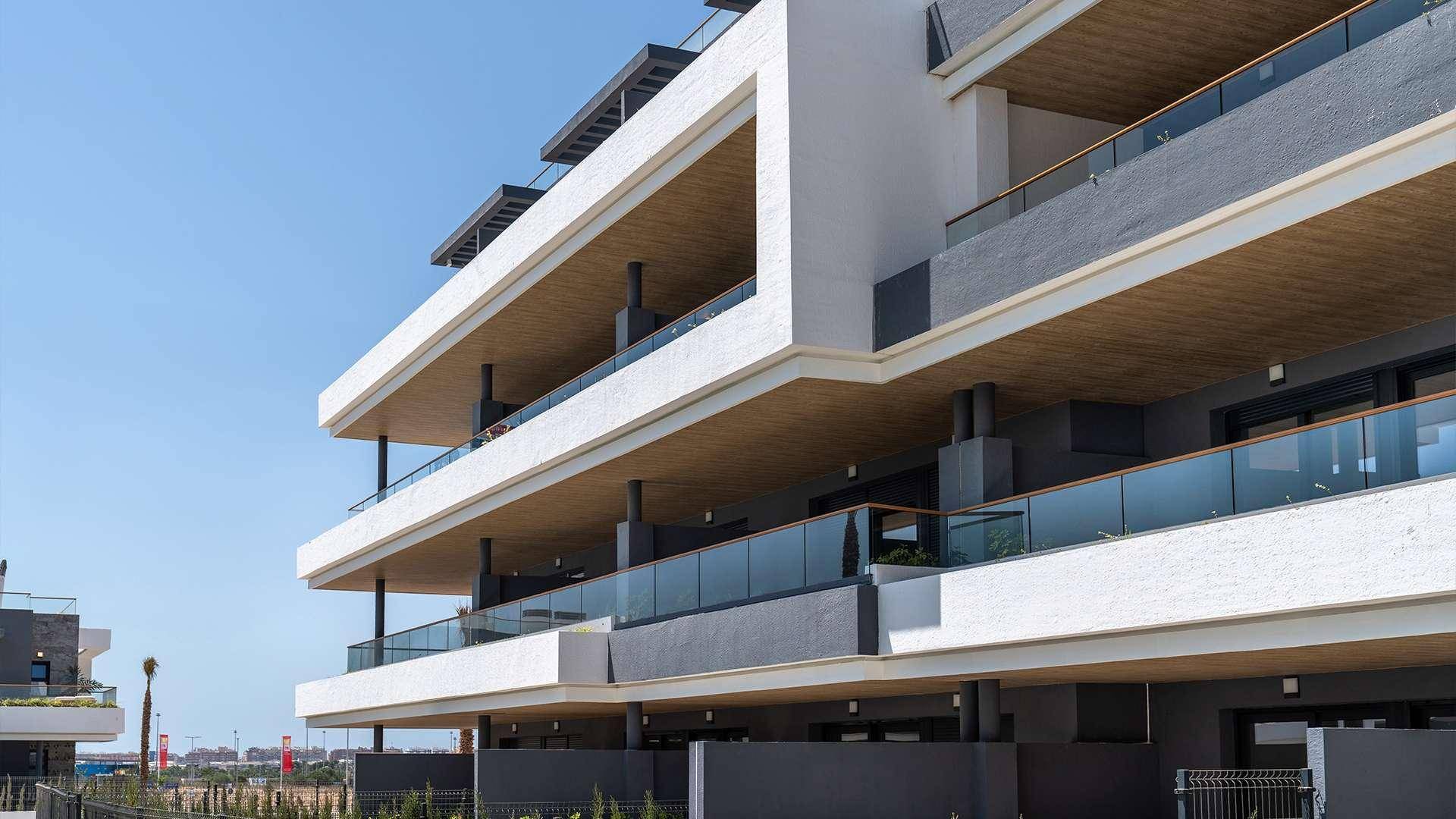 Detailansicht der modernen Architektur eines Apartmentgebäudes mit breiten Balkonen und Glasgeländern.