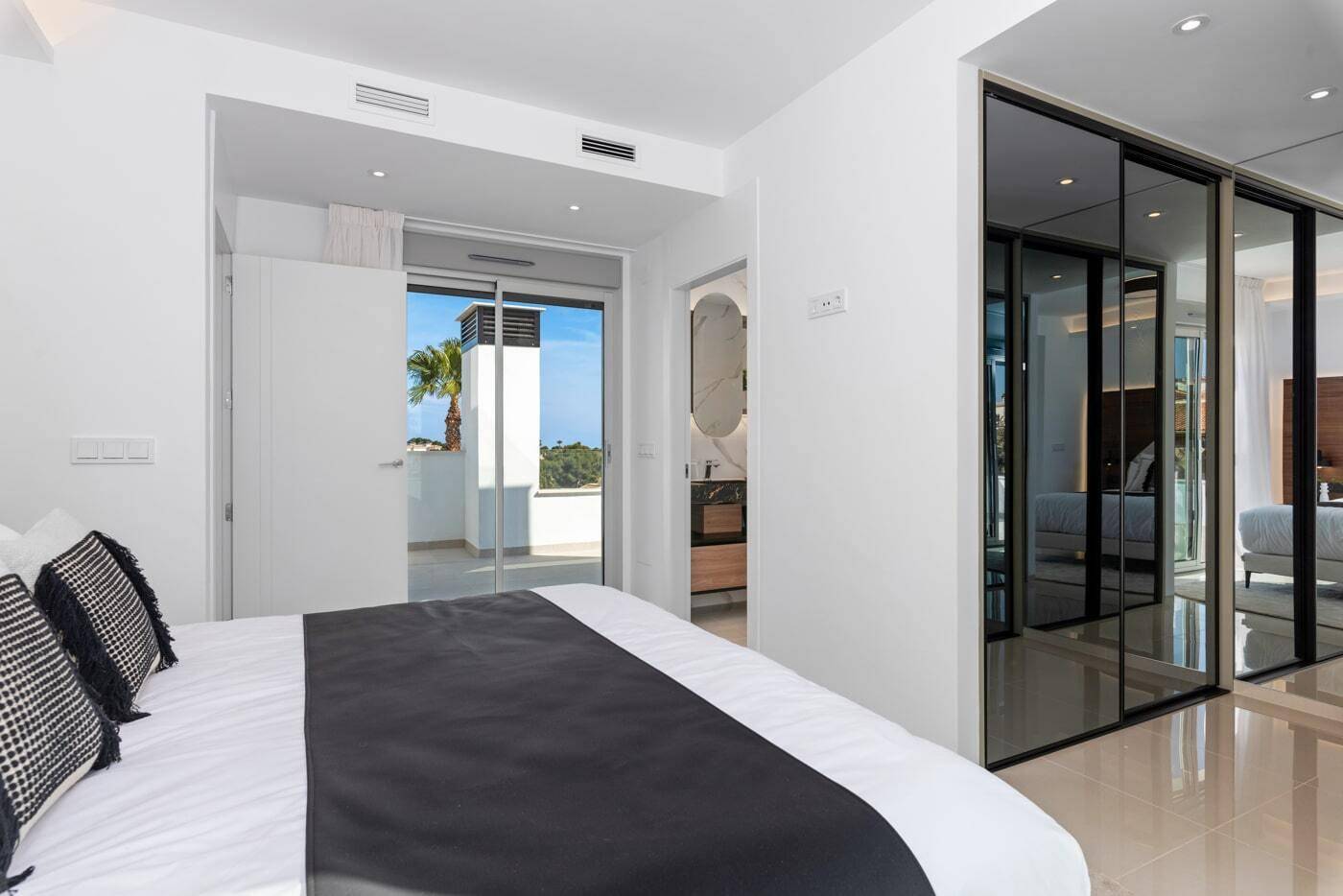 Schlafzimmer mit modernen Spiegelschränken und Blick auf den Außenbereich.