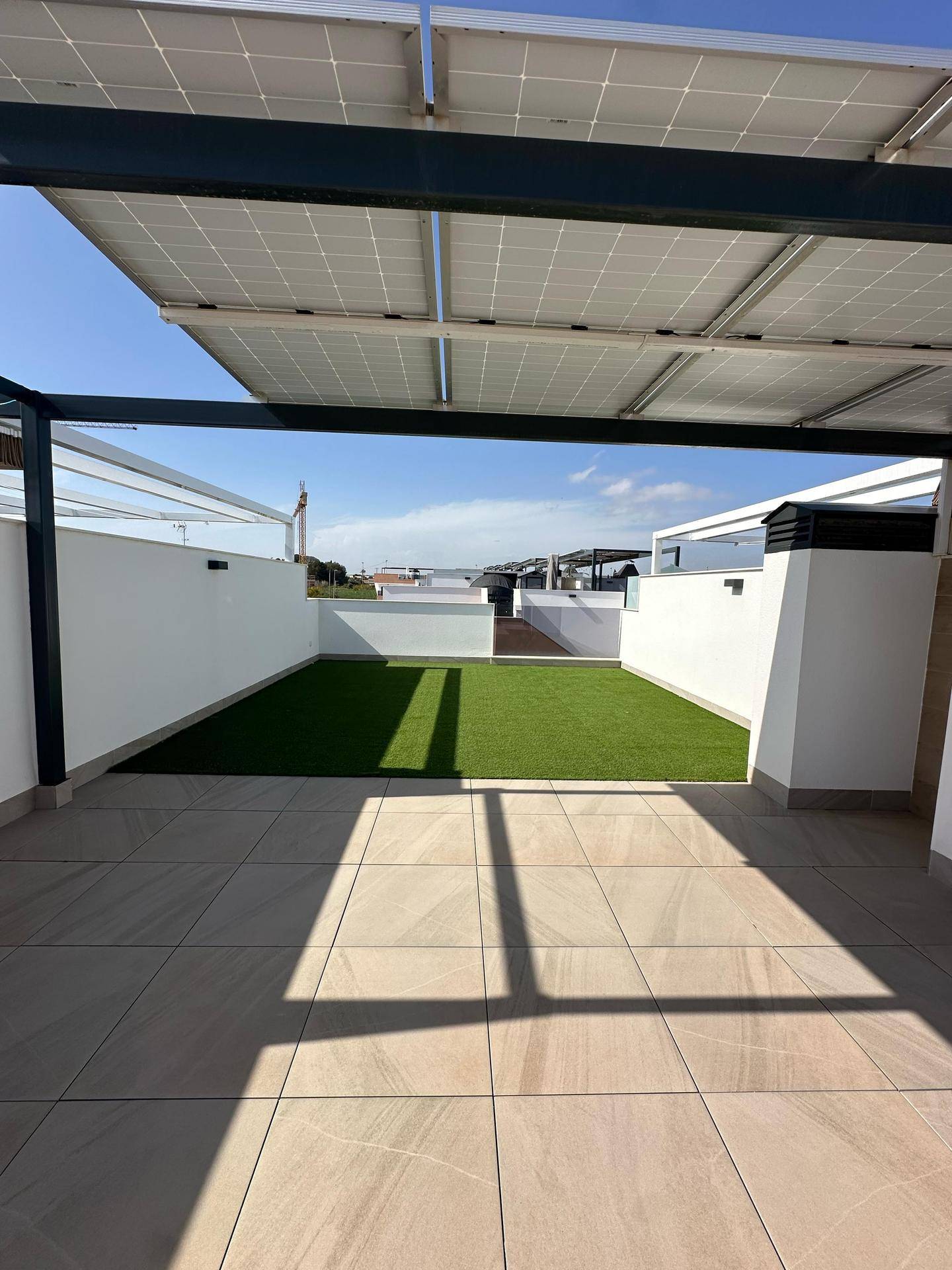 Helle Dachterrasse mit Kunstrasenfläche, Fliesenboden und schattenspendenden Solarpaneelen.