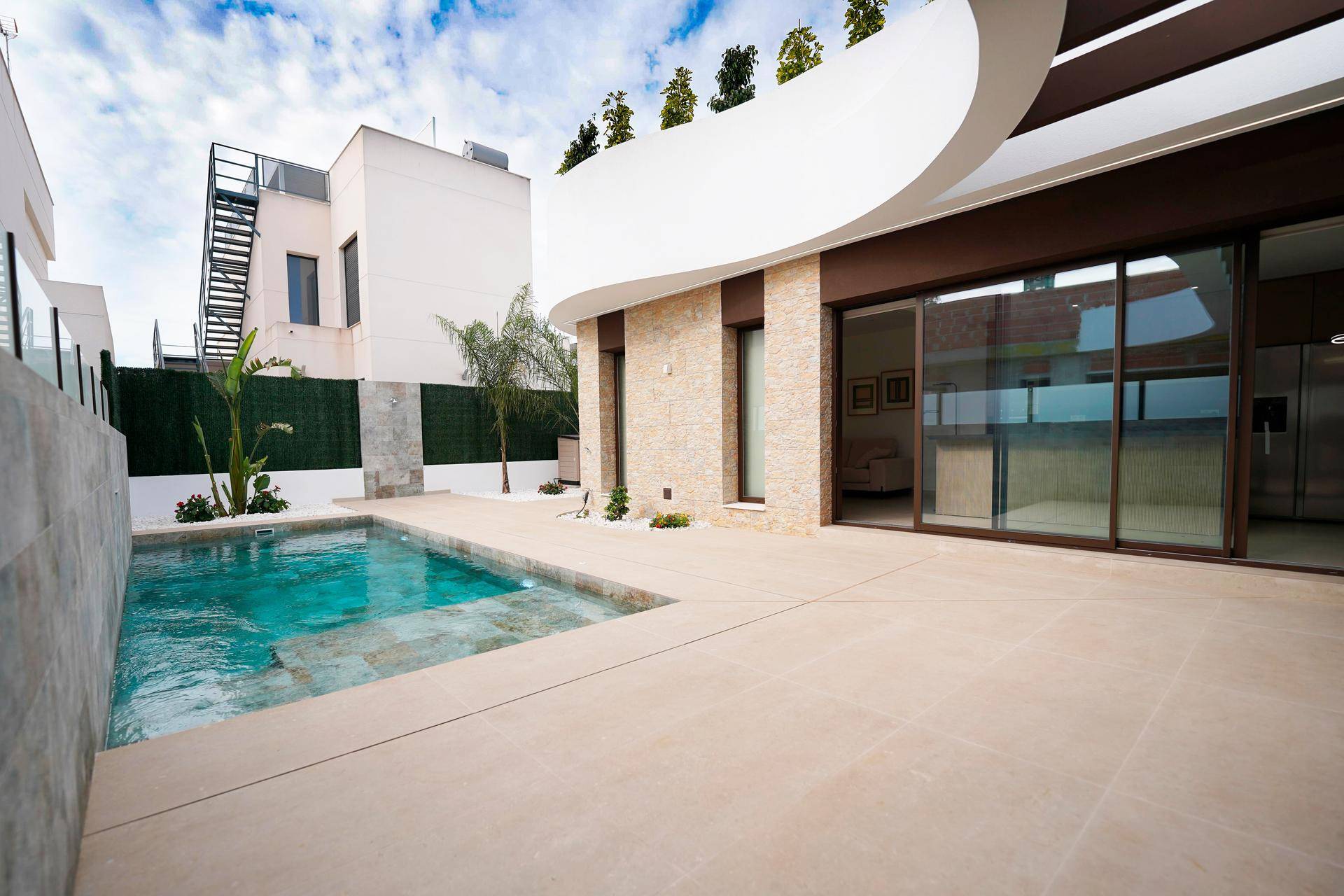 Außenansicht der modernen Villa mit Poolbereich und angrenzender Terrasse, umgeben von einer grünen Hecke.