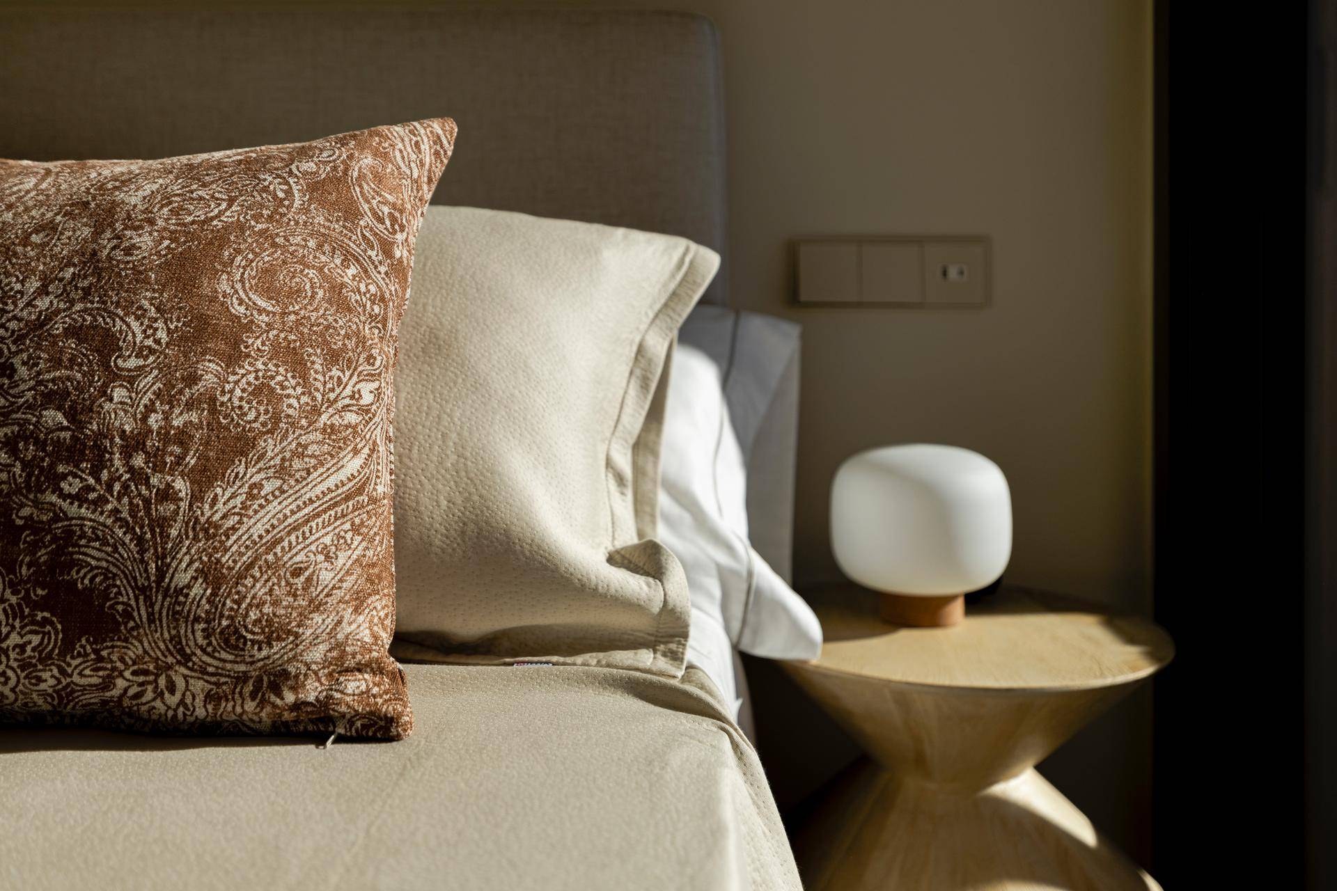 Detailaufnahme eines Nachttisches mit Lampe und dekorativen Kissen im Schlafzimmer.