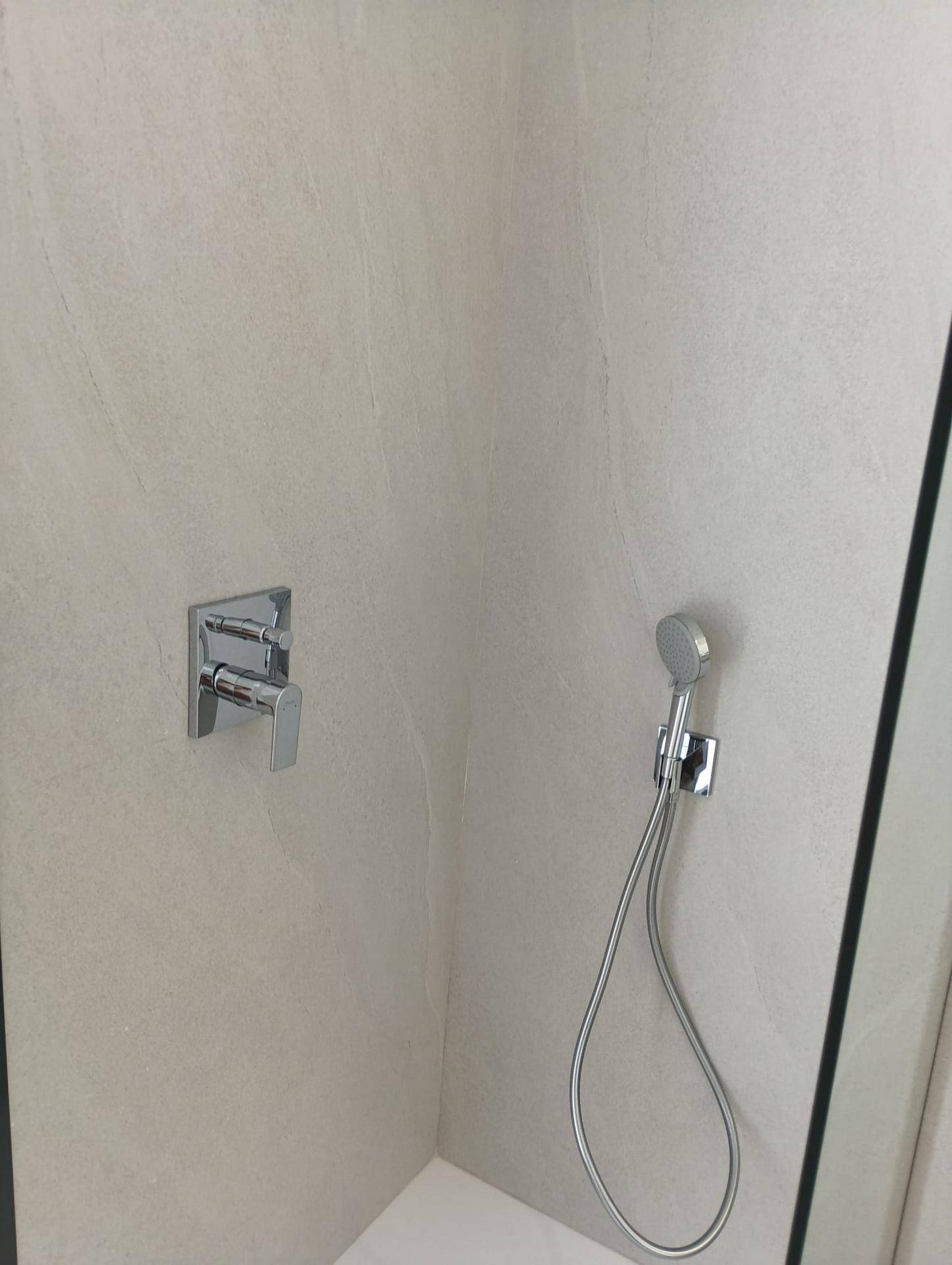 Moderne Duscharmatur und Handbrause in einer hell gefliesten Duschkabine.