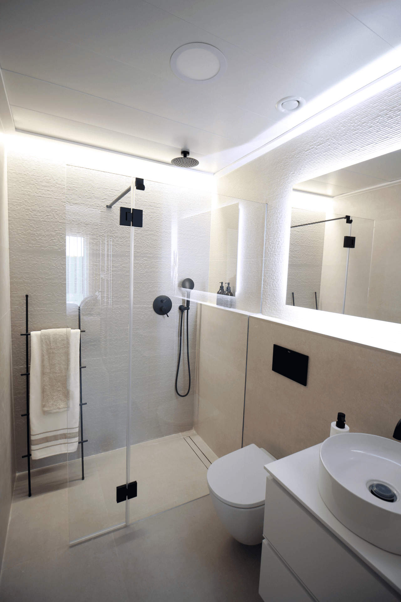 Modernes Badezimmer mit begehbarer Dusche, Wand-WC und beleuchtetem Spiegel.