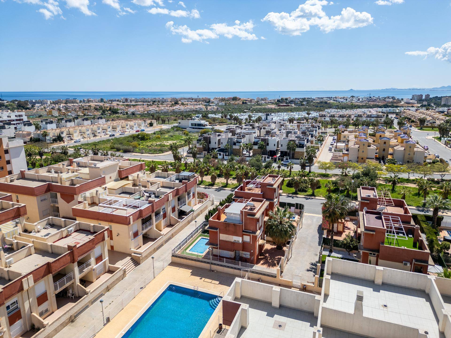 Panoramablick auf den Wohnkomplex mit Pool im Vordergrund und dem Meer in der Ferne.