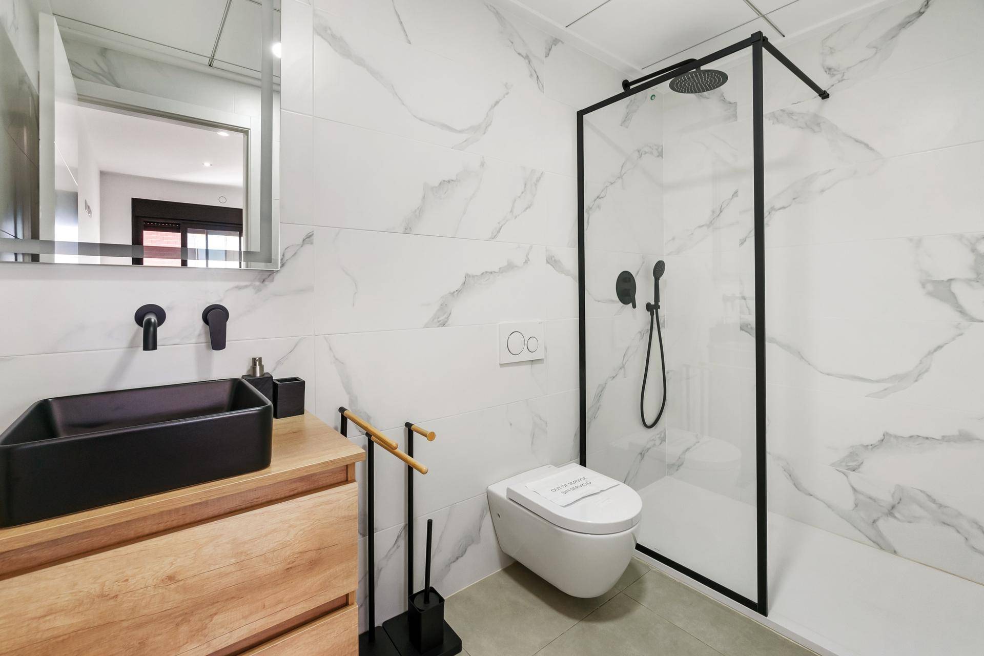 Modernes Badezimmer mit begehbarer Dusche, schwarzem Waschbecken und weißen Marmorfliesen.