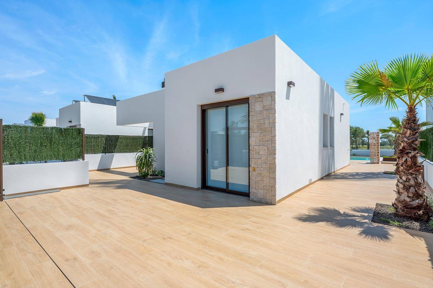 Moderne Hausfassade mit Steinelementen und einer großzügigen Holzterrasse.