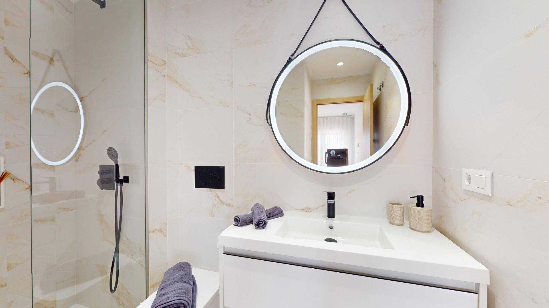 Modernes Badezimmer mit beleuchtetem Spiegel, Waschtisch und einer geräumigen Duschkabine.