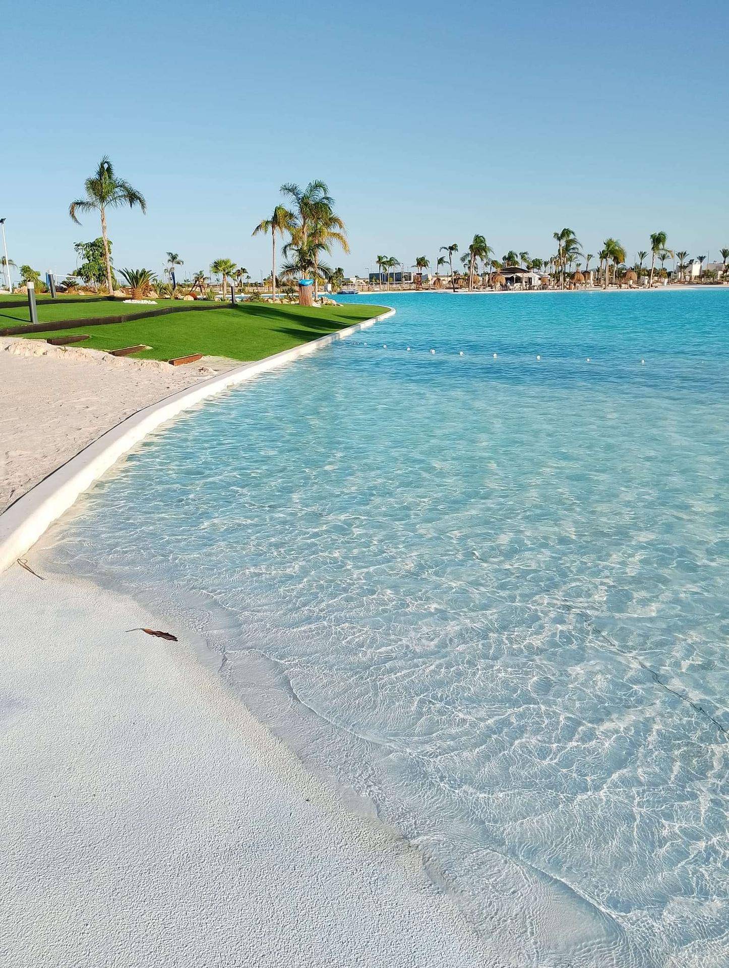 Künstliche Lagune mit Sandstrand und flachem Uferbereich, umgeben von Grünflächen.