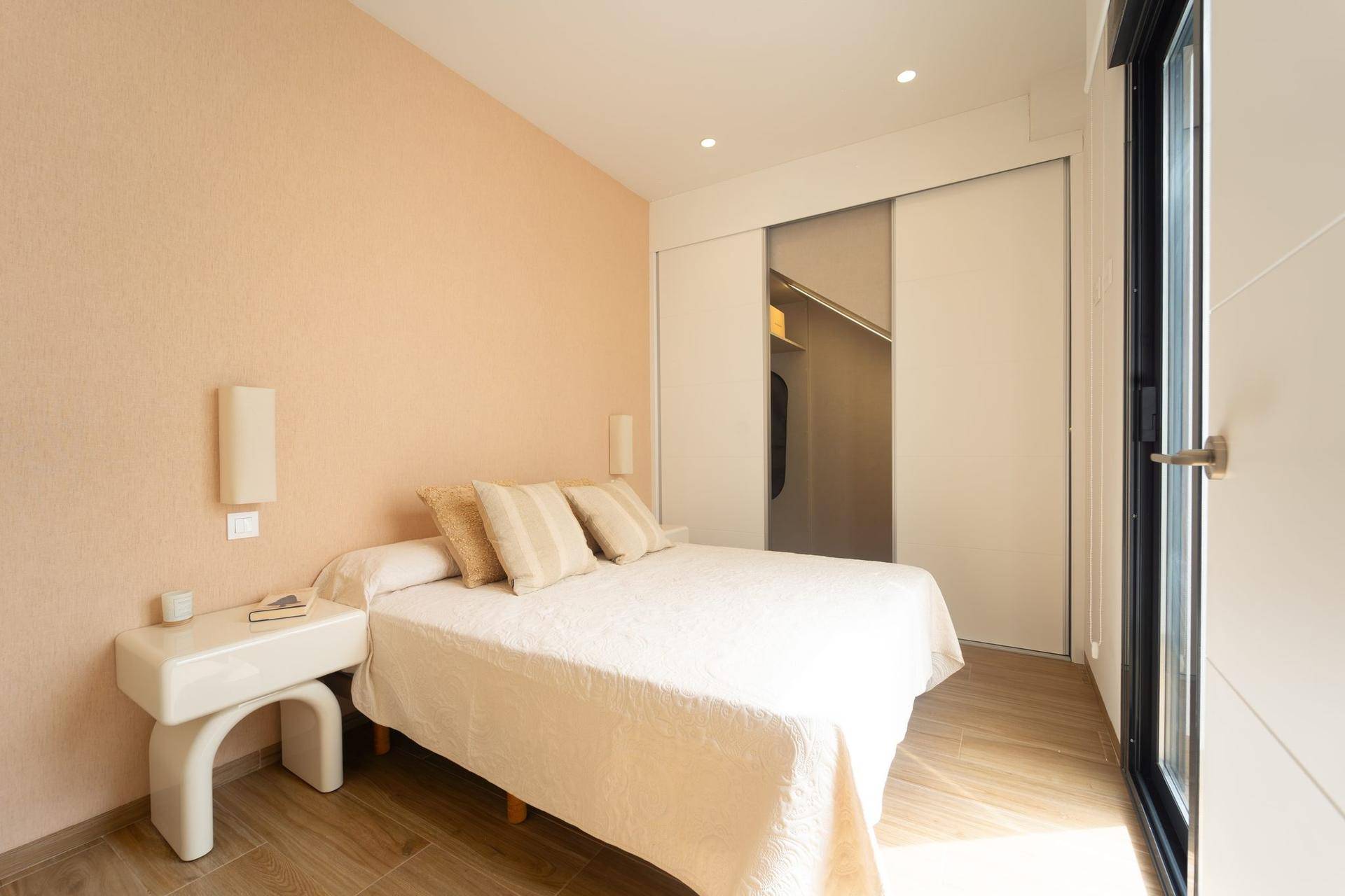 Helles Schlafzimmer mit Doppelbett, Einbauschränken und Zugang zu einem Außenbereich.