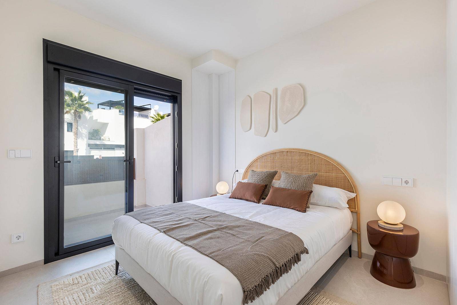 Helles Schlafzimmer mit Doppelbett, Rattan-Kopfteil und Zugang zu einem Außenbereich.