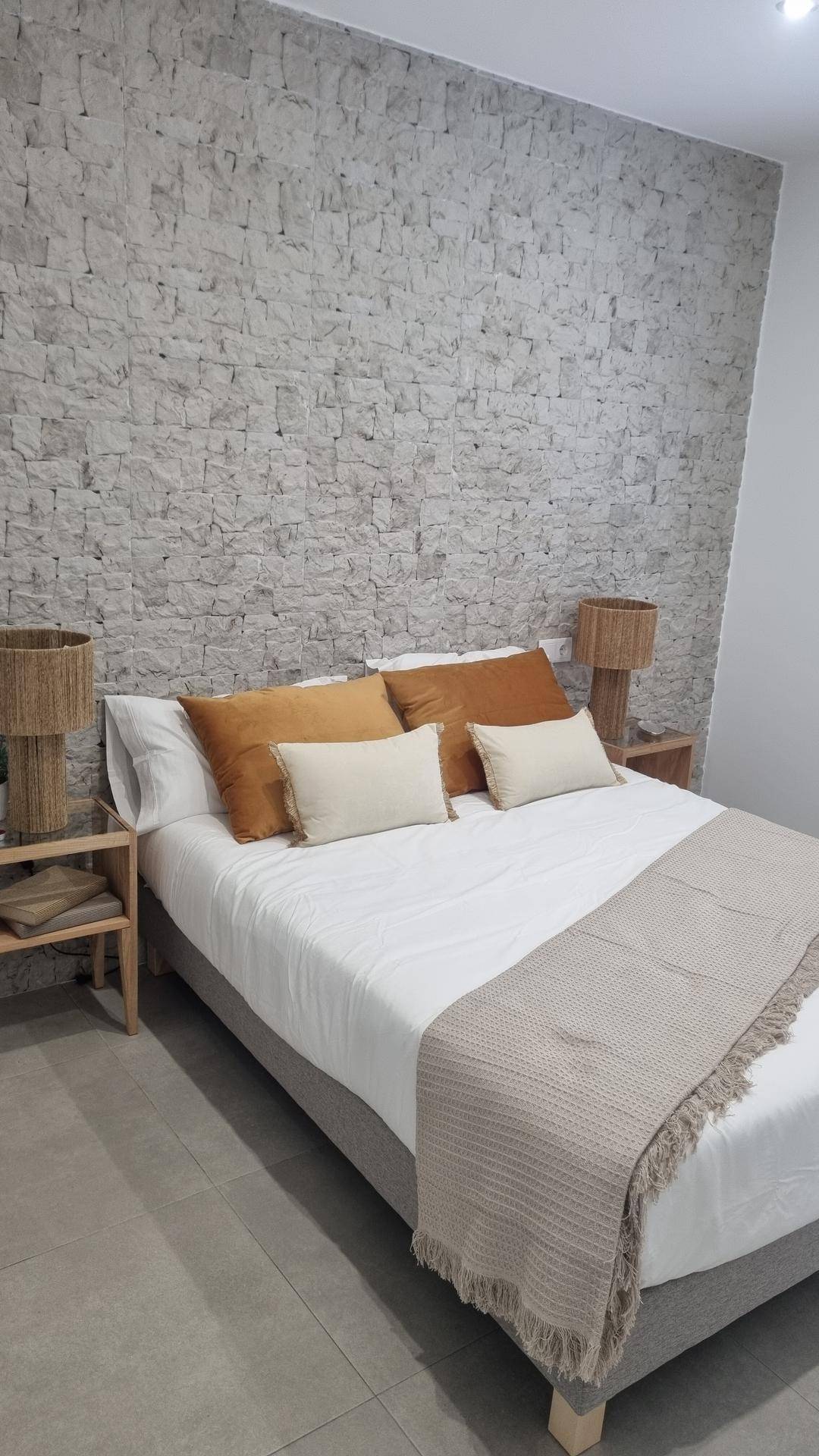 Schlafzimmer mit strukturierter Steinwand, Doppelbett und modernen Nachttischen.