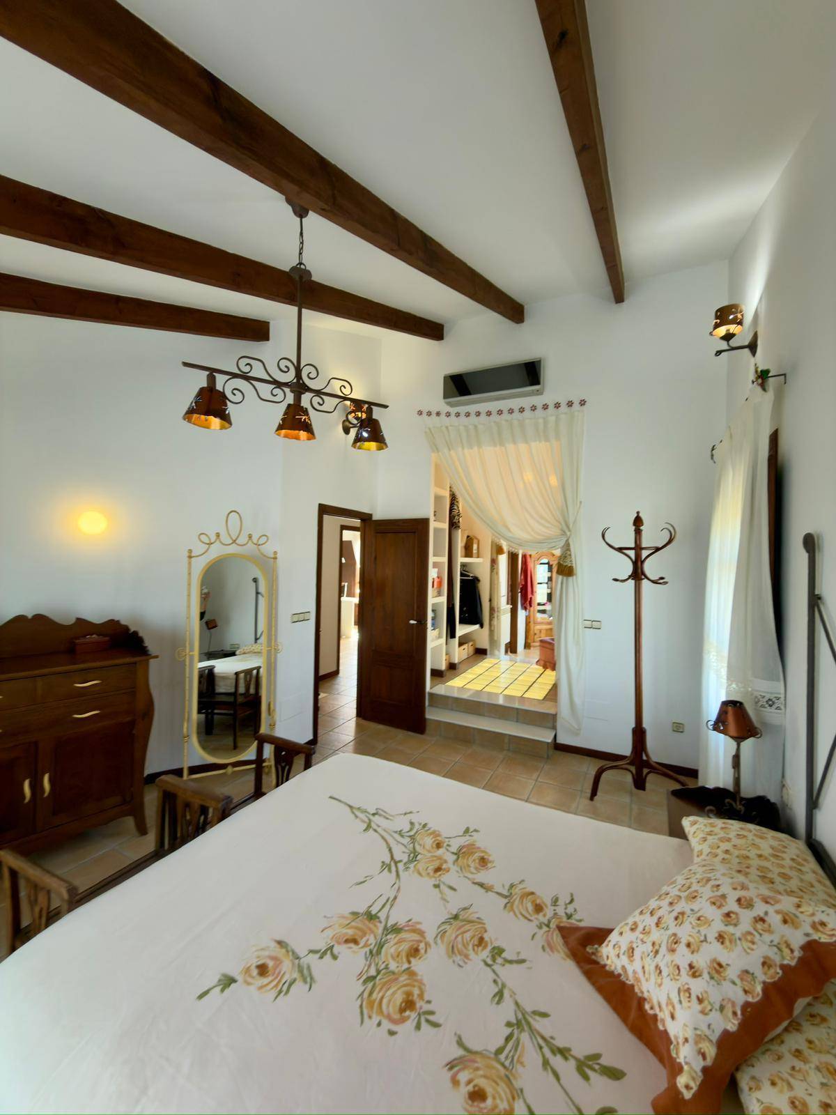 Schlafzimmer mit traditionellem Ambiente, Holzbalken und offenem Zugang zum Ankleidebereich.