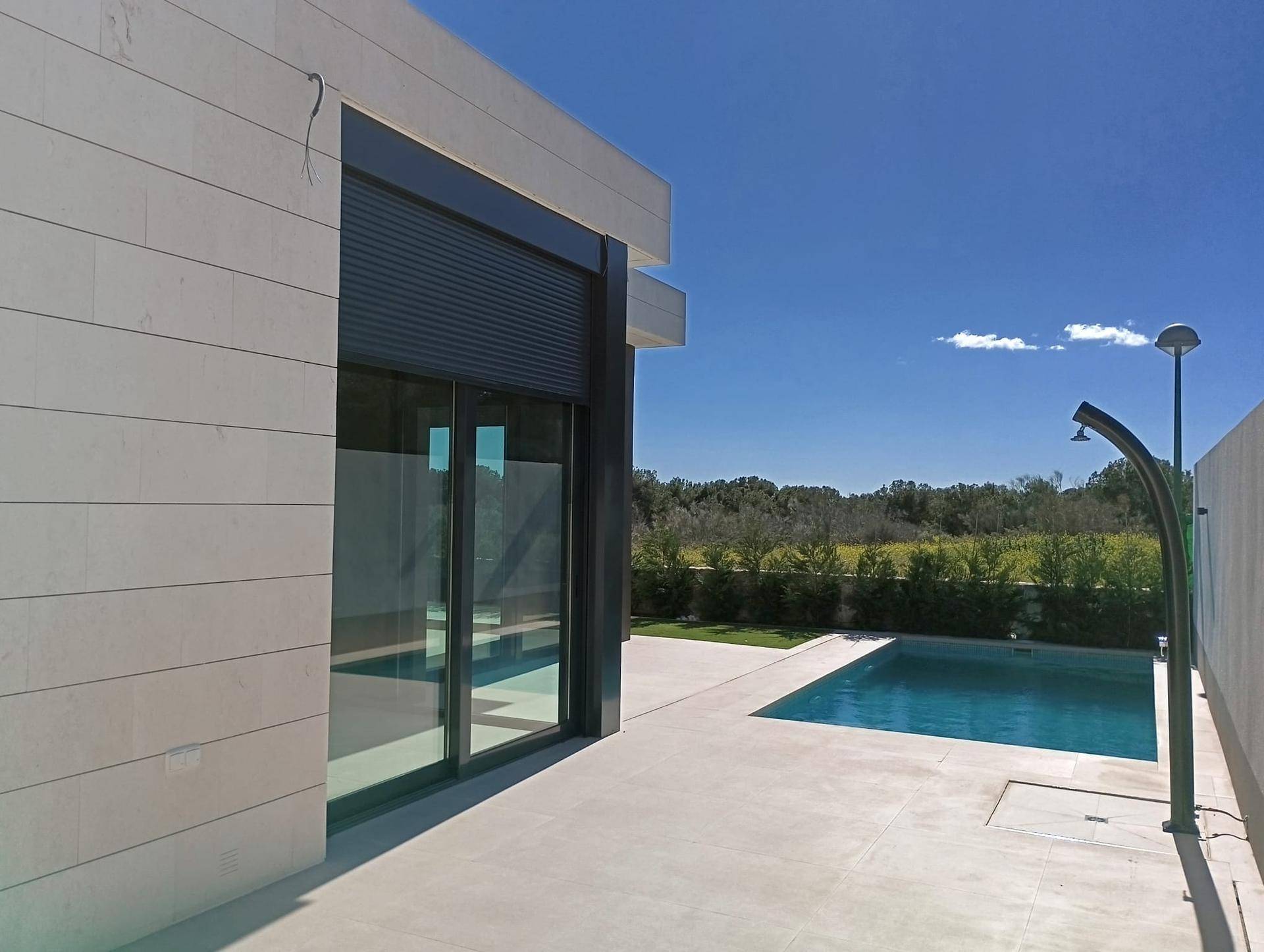 Moderne Villa mit großen Glasfronten und einem einladenden Poolbereich unter blauem Himmel.