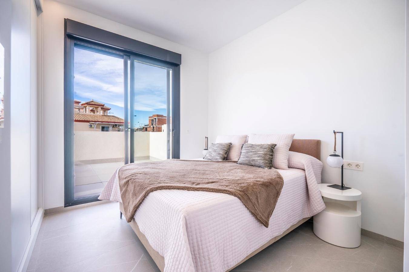 Helles Schlafzimmer mit Doppelbett, minimalistischer Einrichtung und Zugang zu einem Balkon oder einer Terrasse.