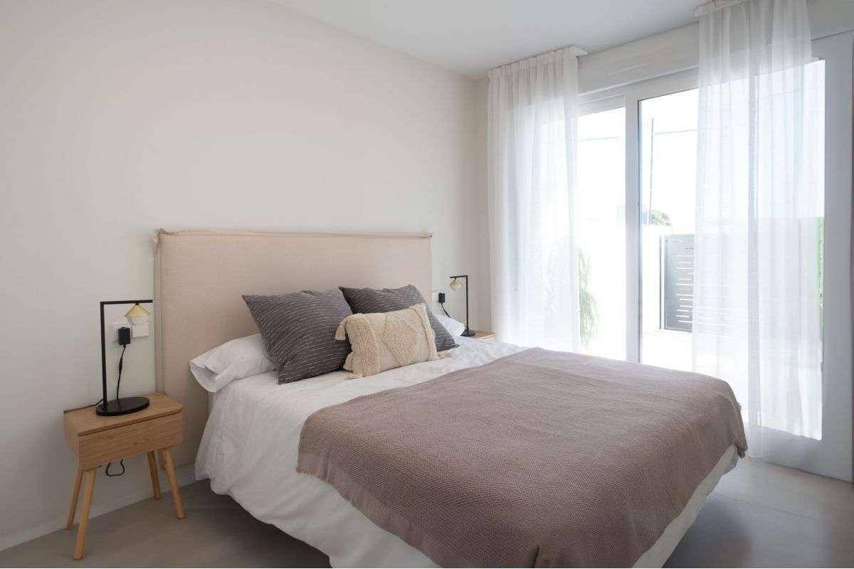 Helles Schlafzimmer mit Doppelbett, Nachttischen und großen Fenstern mit transparenten Vorhängen.