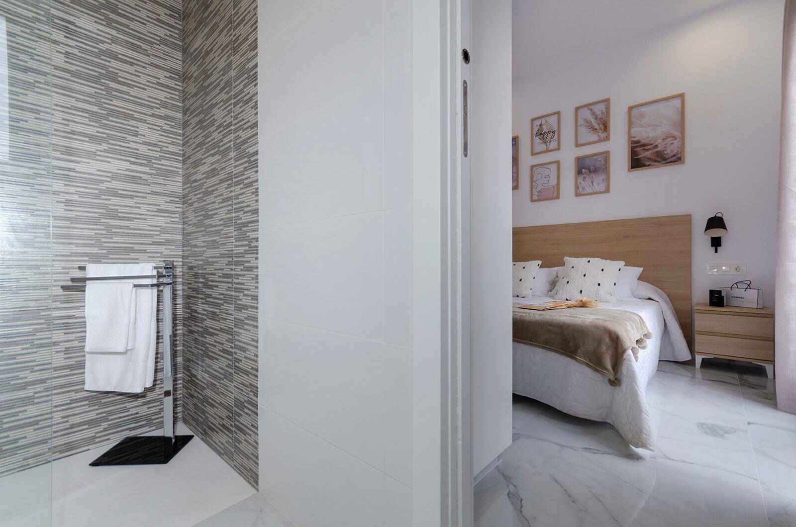 Modernes Badezimmer mit begehbarer Dusche und Blick in ein helles Schlafzimmer.