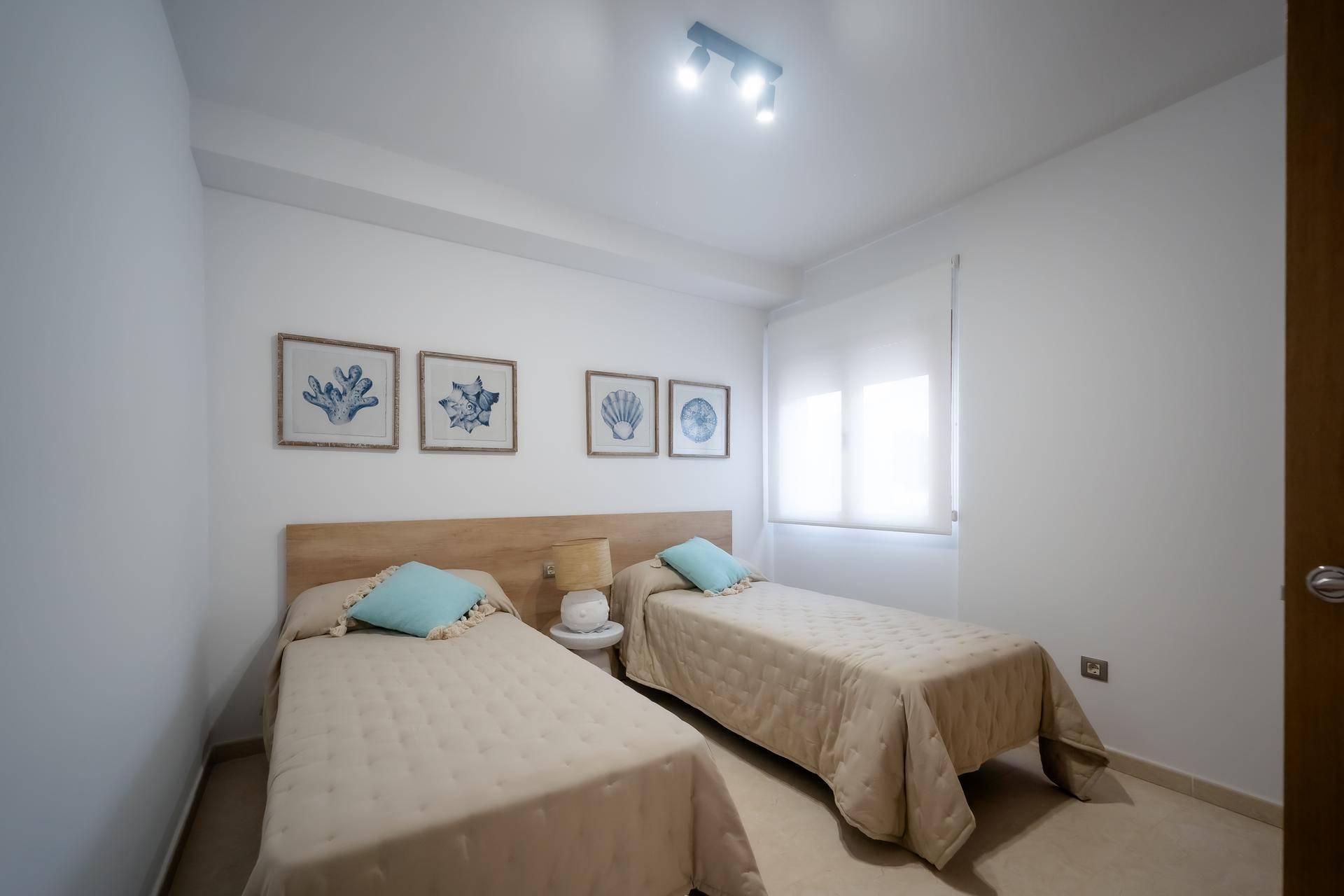 Schlafzimmer mit zwei Einzelbetten, Fenster und einfacher, maritimer Dekoration.
