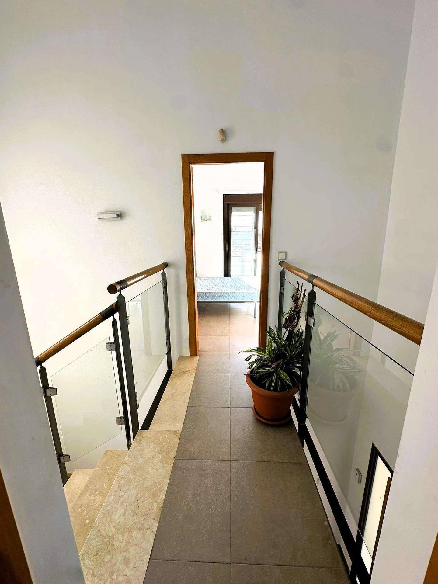 Heller Flur mit Treppe, Glasgeländer und einem Blick in ein angrenzendes Schlafzimmer.