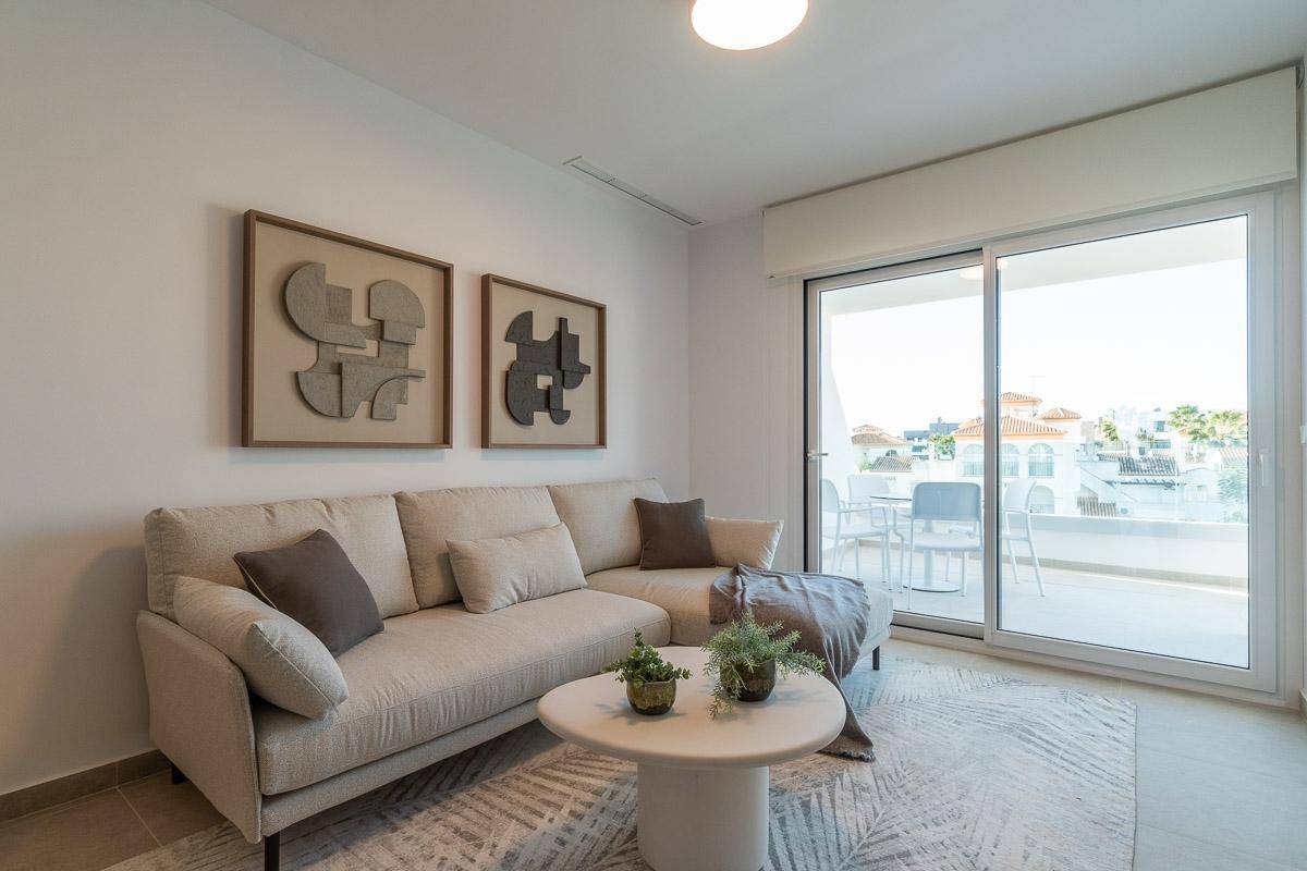 Helles Wohnzimmer mit beigem Sofa, Couchtisch und Zugang zu einem Balkon mit Blick auf die Umgebung.
