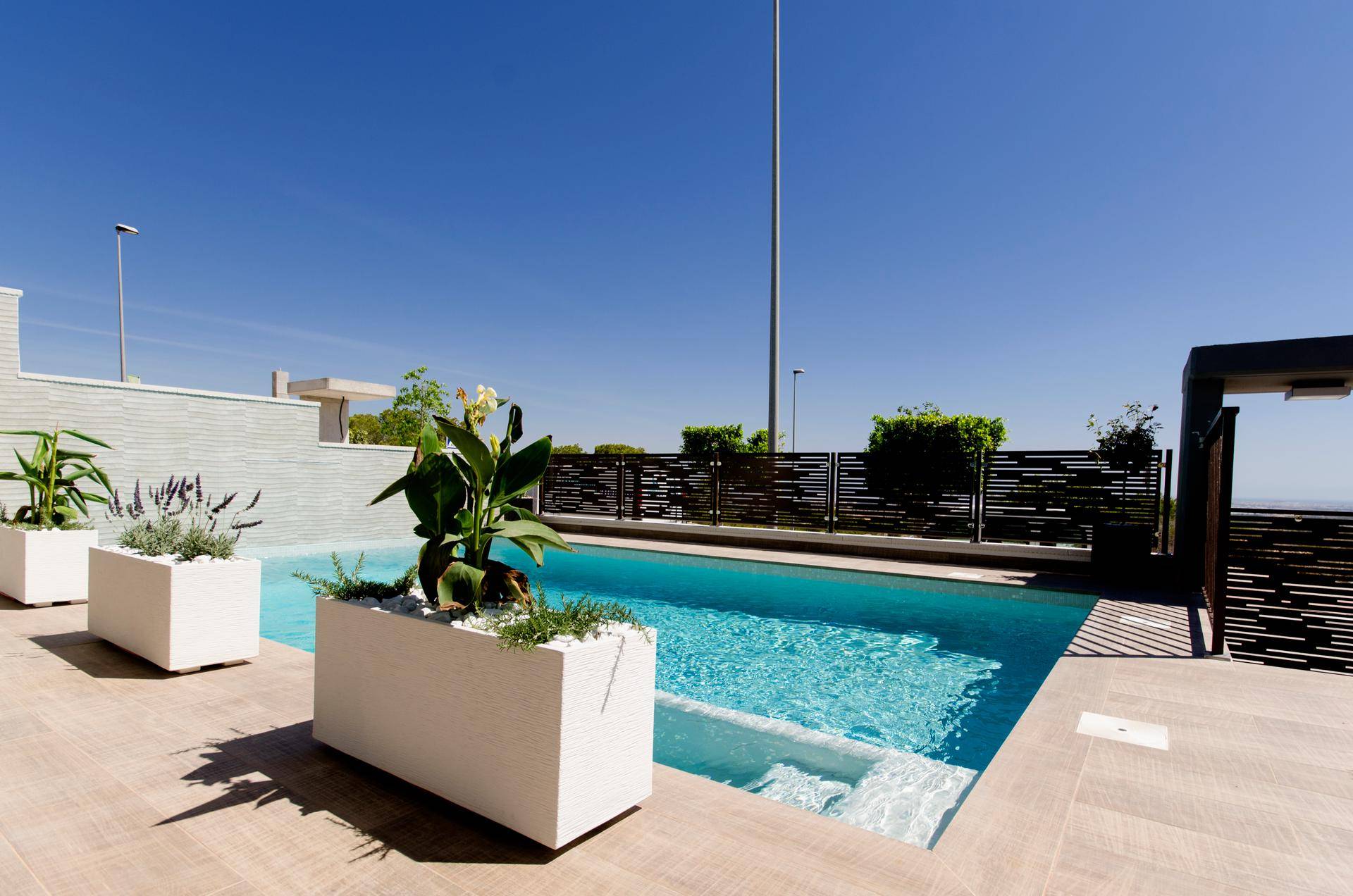 Heller Poolbereich mit modernen Pflanzkübeln und Holzdeck unter strahlend blauem Himmel.