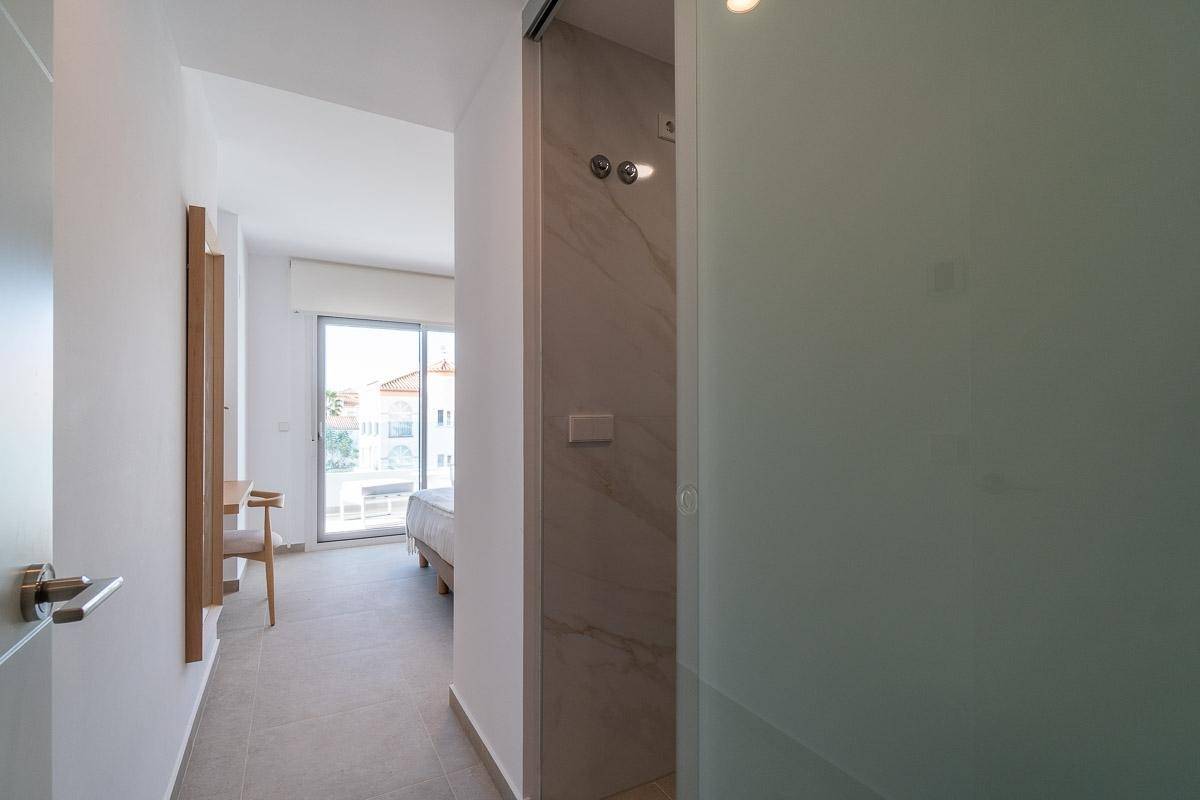 Heller Flur mit Blick auf ein Schlafzimmer und ein Badezimmer mit Glasschiebetür.
