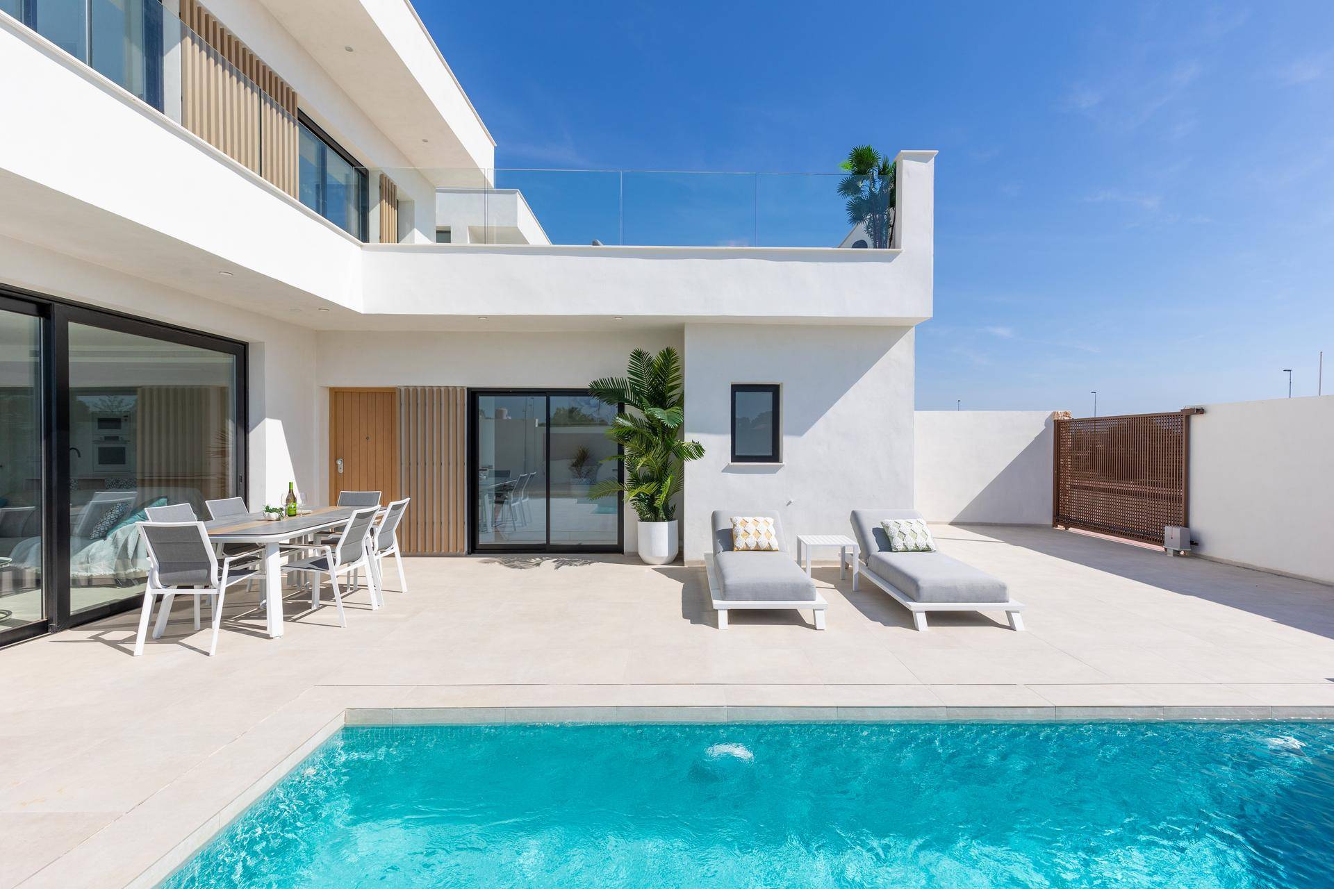 Sonniger Außenbereich mit Pool, Liegestühlen und Esstisch neben der modernen Villa.