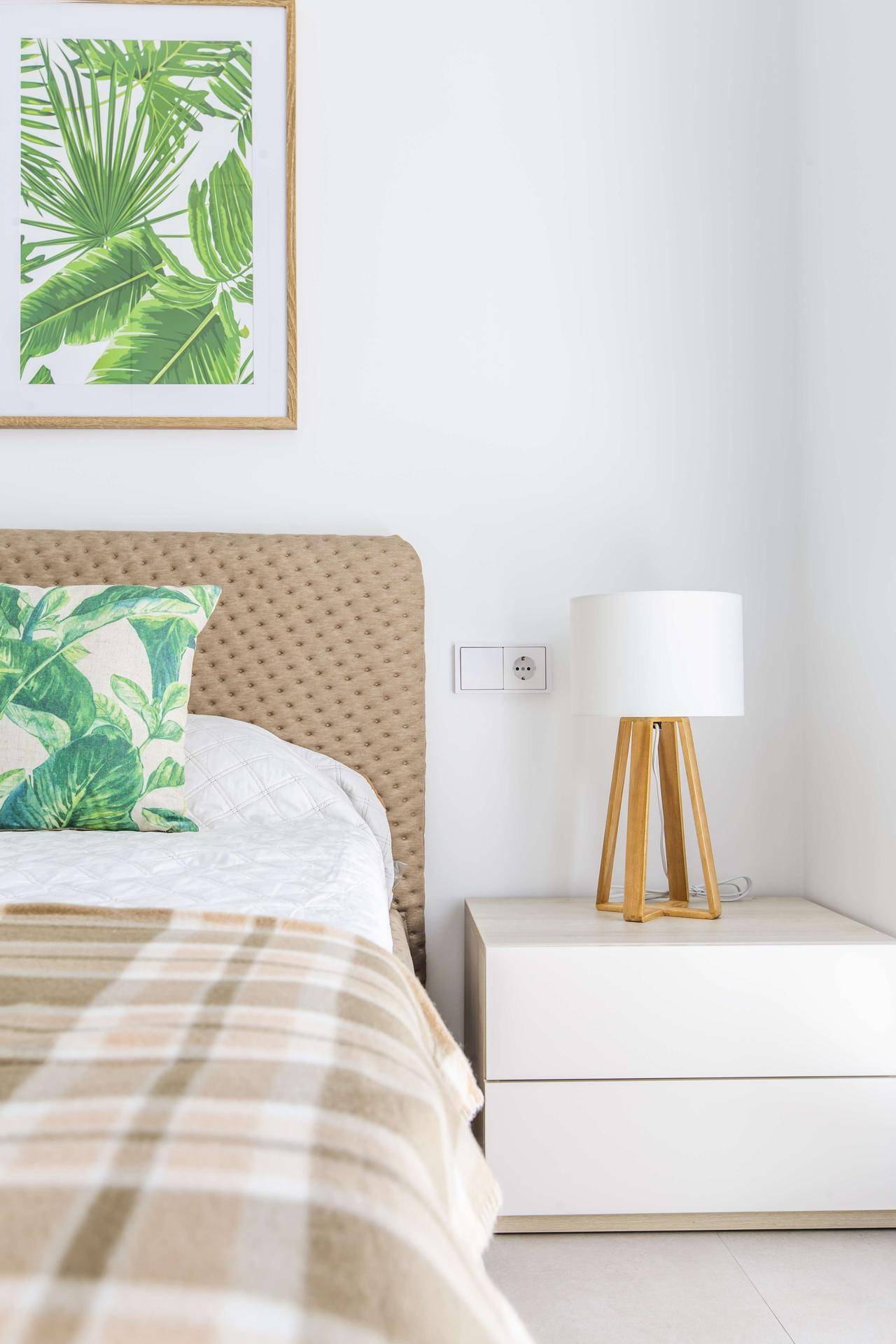 Helles Schlafzimmer mit beigem Kopfteil, modernem Nachttisch und tropischem Wandbild.