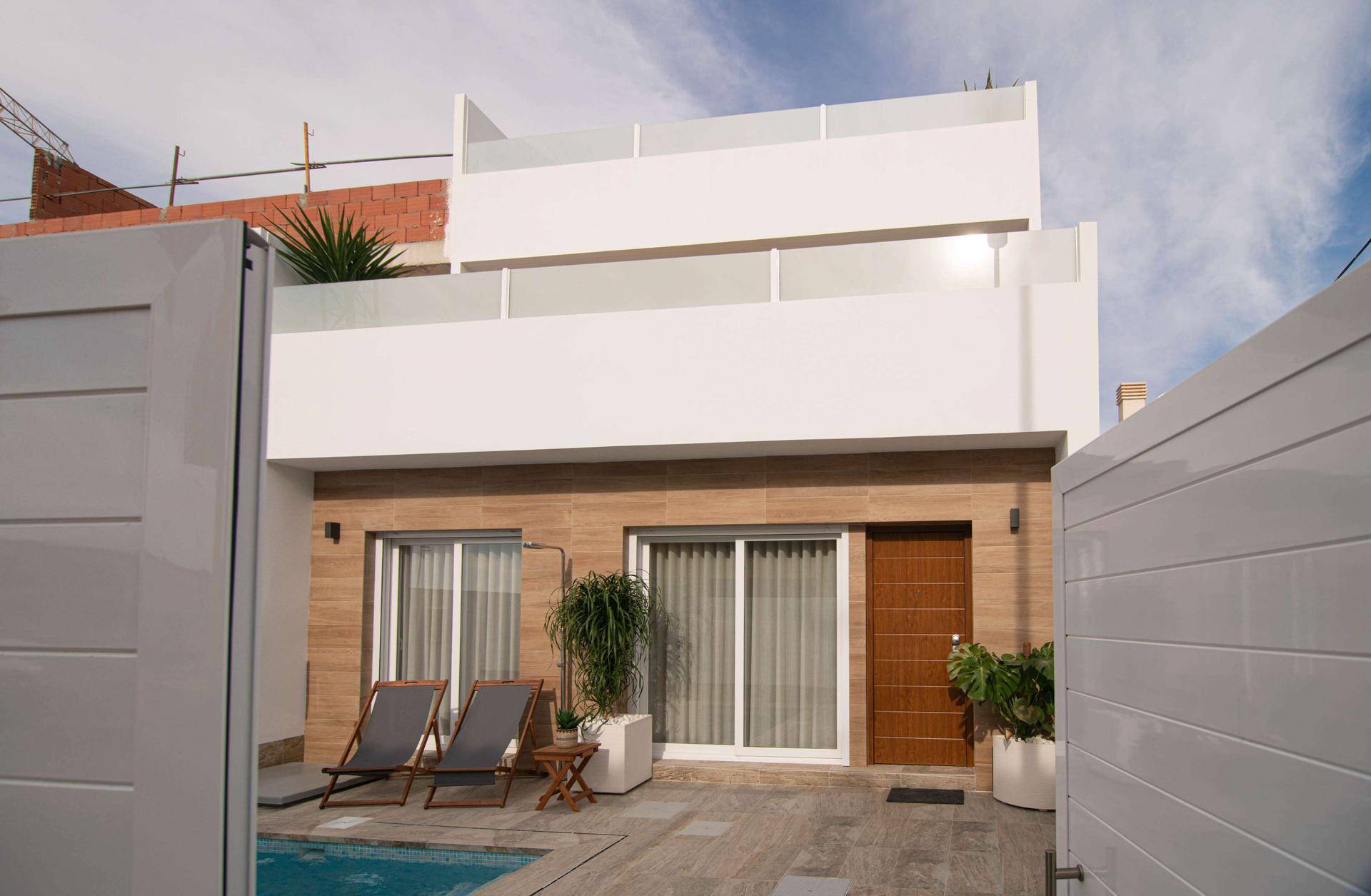 Eingangsbereich des modernen Hauses mit Pool, Liegestühlen und einer weißen Zufahrt.