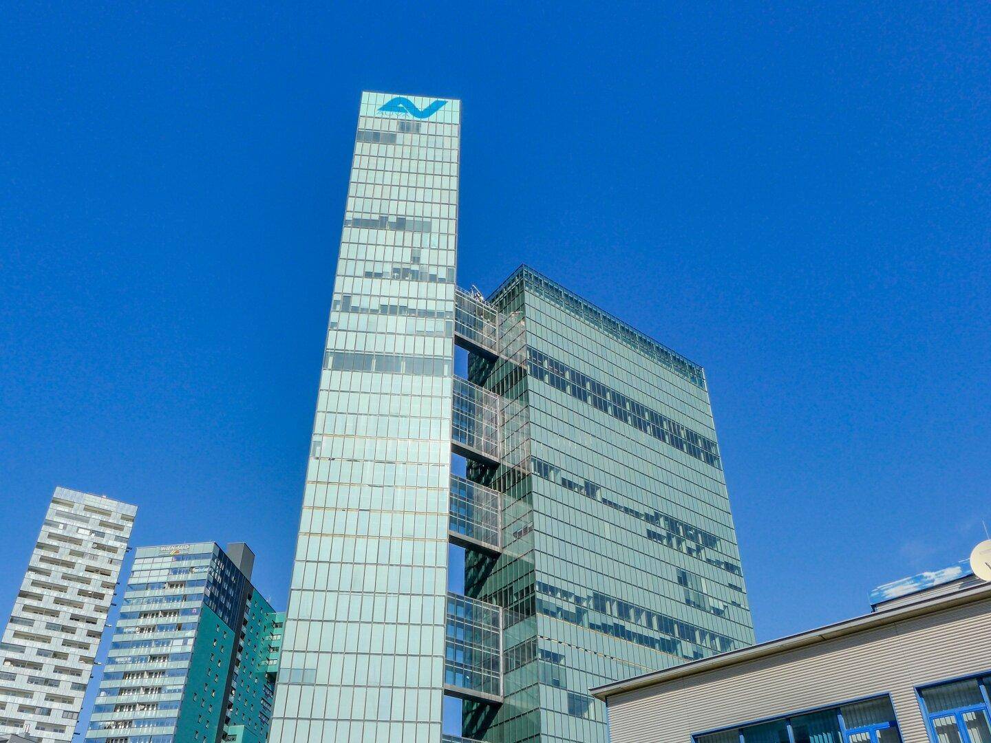 Moderner Wolkenkratzer mit Glasfassade und markantem Logo unter strahlend blauem Himmel.