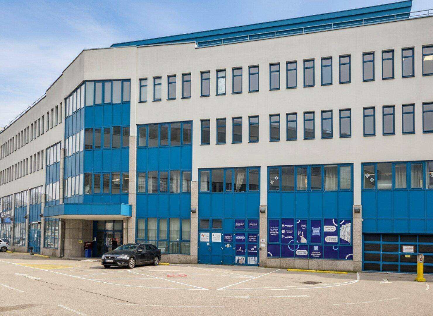 Ansicht eines modernen Bürogebäudes mit blauen Fensterrahmen und einem Eingangsbereich.