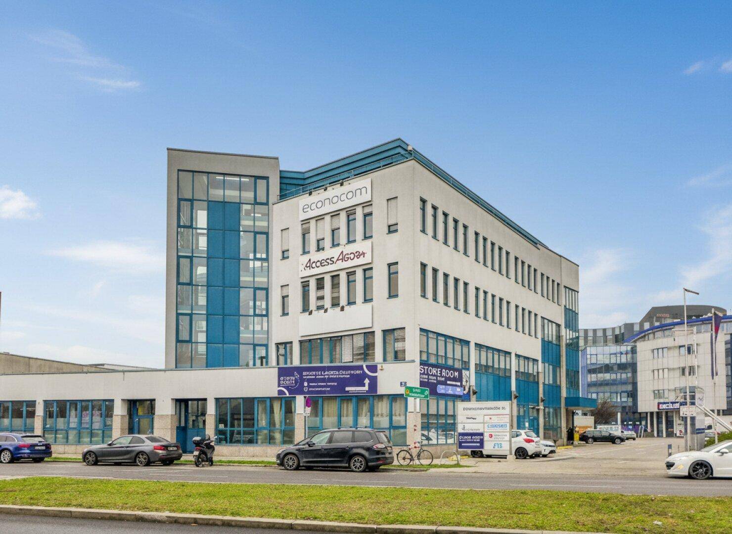 Modernes Bürogebäude mit blauen Akzenten, großen Glasflächen und Parkplätzen davor.