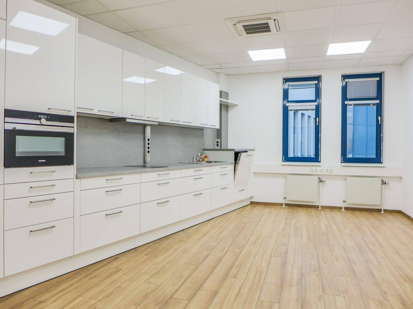 Moderne Einbauküche mit weißen Hochglanzschränken, integrierten Geräten und Holzoptik-Boden.