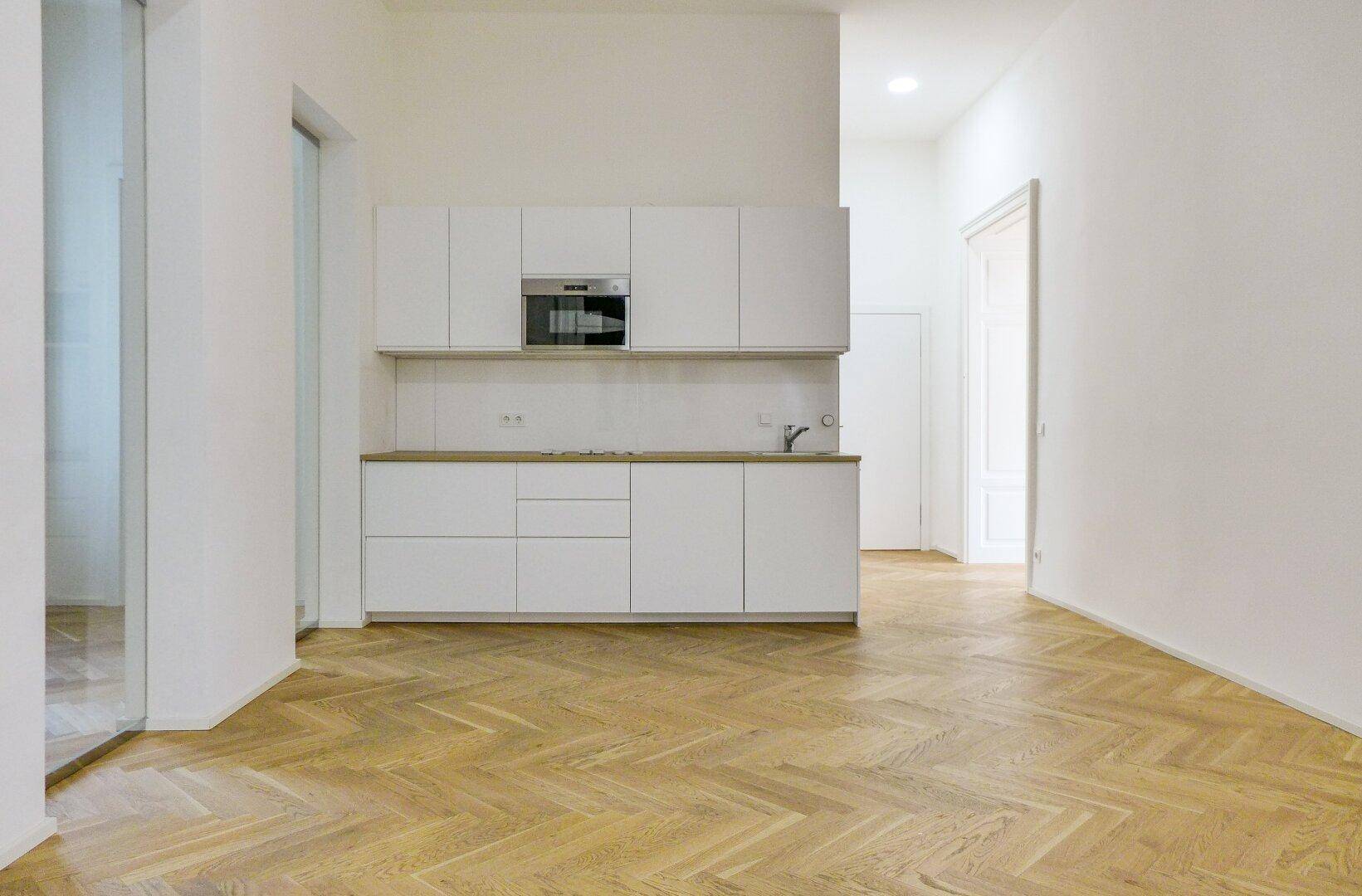 Offene Küche mit minimalistischen weißen Schränken und Holzarbeitsplatte, verbunden mit einem hellen Wohnbereich.