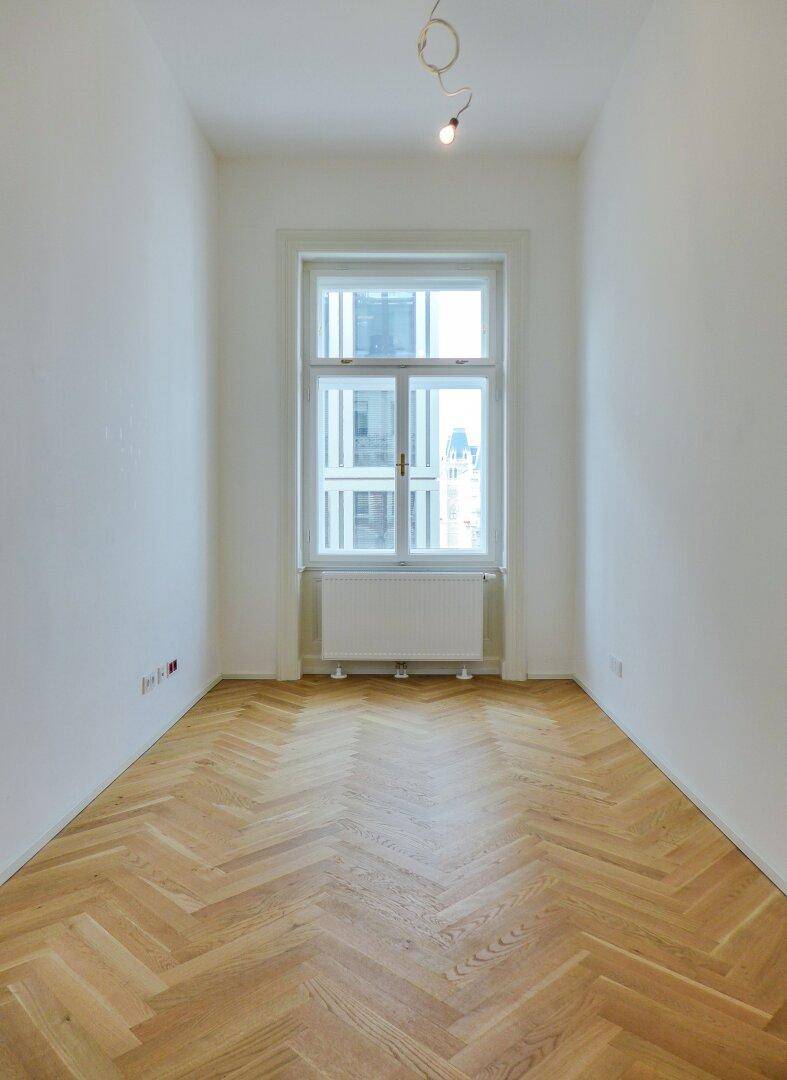 Schmaler Raum mit einem großen Fenster und Fischgrätparkett, bietet eine helle und ruhige Atmosphäre.