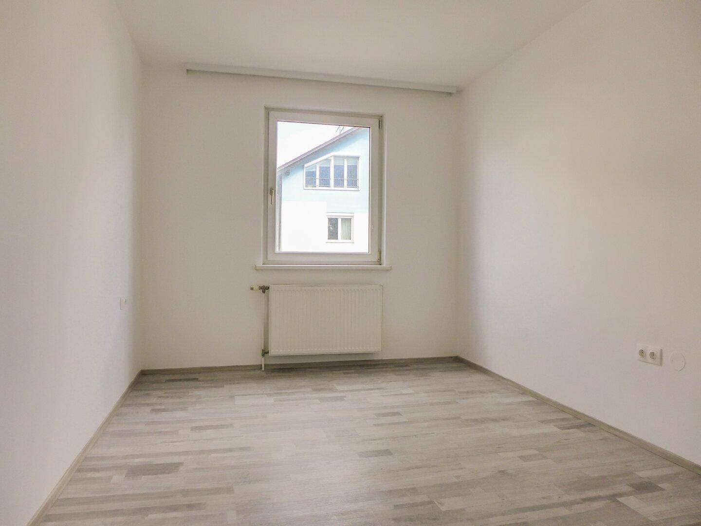 Helles Schlafzimmer mit Fenster und Heizkörper, ideal für Ruhe und Entspannung.