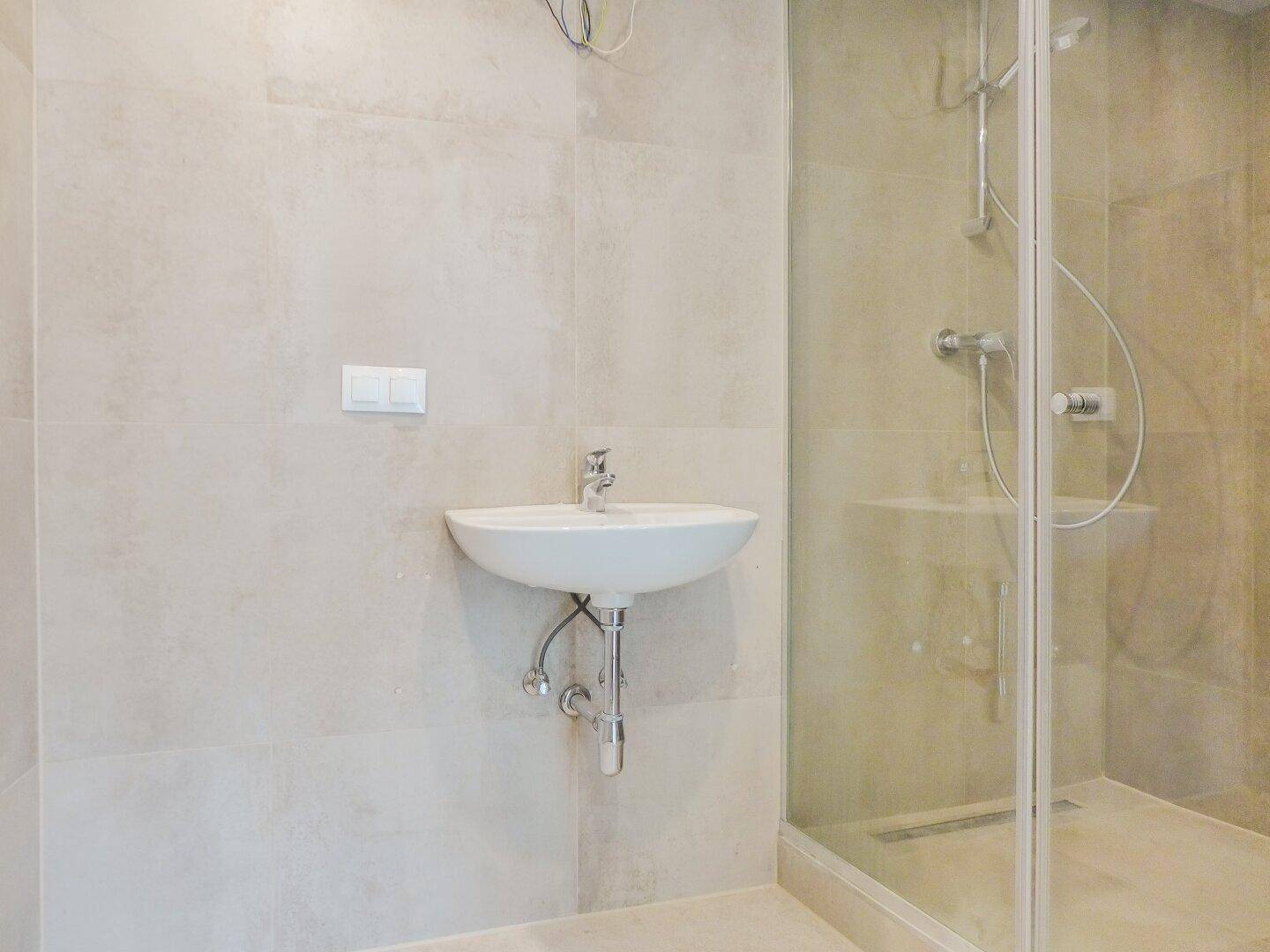 Helles Badezimmer mit modernem Waschbecken und Duschkabine, in neutralen Farbtönen gehalten.