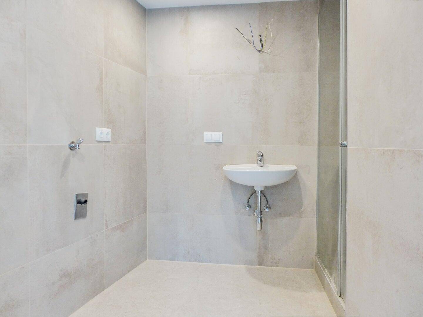 Modern gefliestes Badezimmer mit Waschbecken und Duschbereich, noch unfertig.