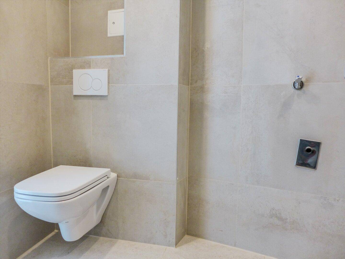 Modernes WC mit wandhängender Toilette und hellen Fliesen, sauber und funktional.