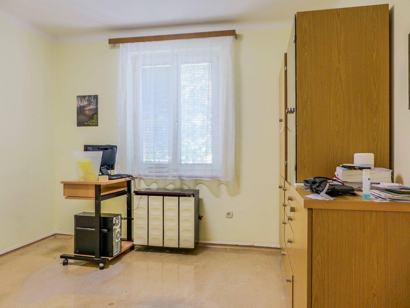 Helles Zimmer mit Schreibtisch, Computer und Holzschränken, ideal als Arbeits- oder Gästezimmer.
