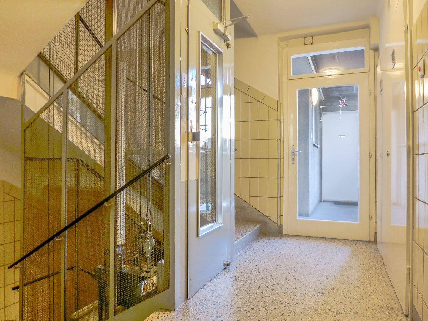 Treppenhaus mit Gittergeländer und einem Aufzug, der den Zugang zu den oberen Etagen ermöglicht.