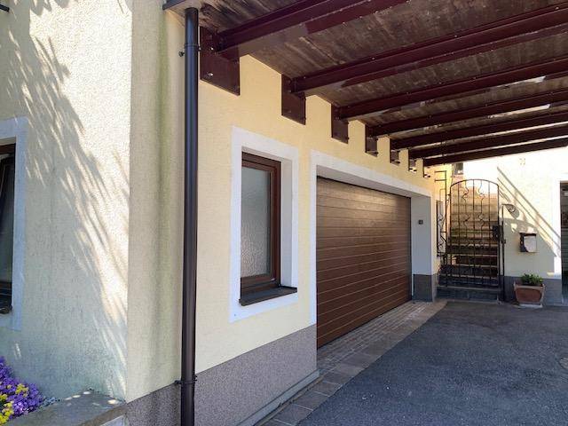 Einzelgarage mit braunem Tor und einem überdachten Carport-Bereich neben dem Haus.