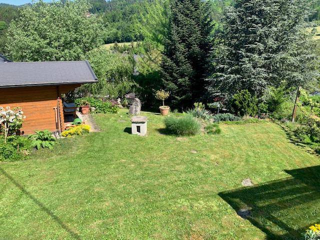 Großer Garten mit Rasen, einem Gartenhaus und verschiedenen Pflanzen, umgeben von Bäumen.