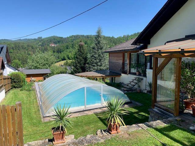 Gartenbereich mit einem überdachten Swimmingpool und Blick auf die umliegende Hügellandschaft.