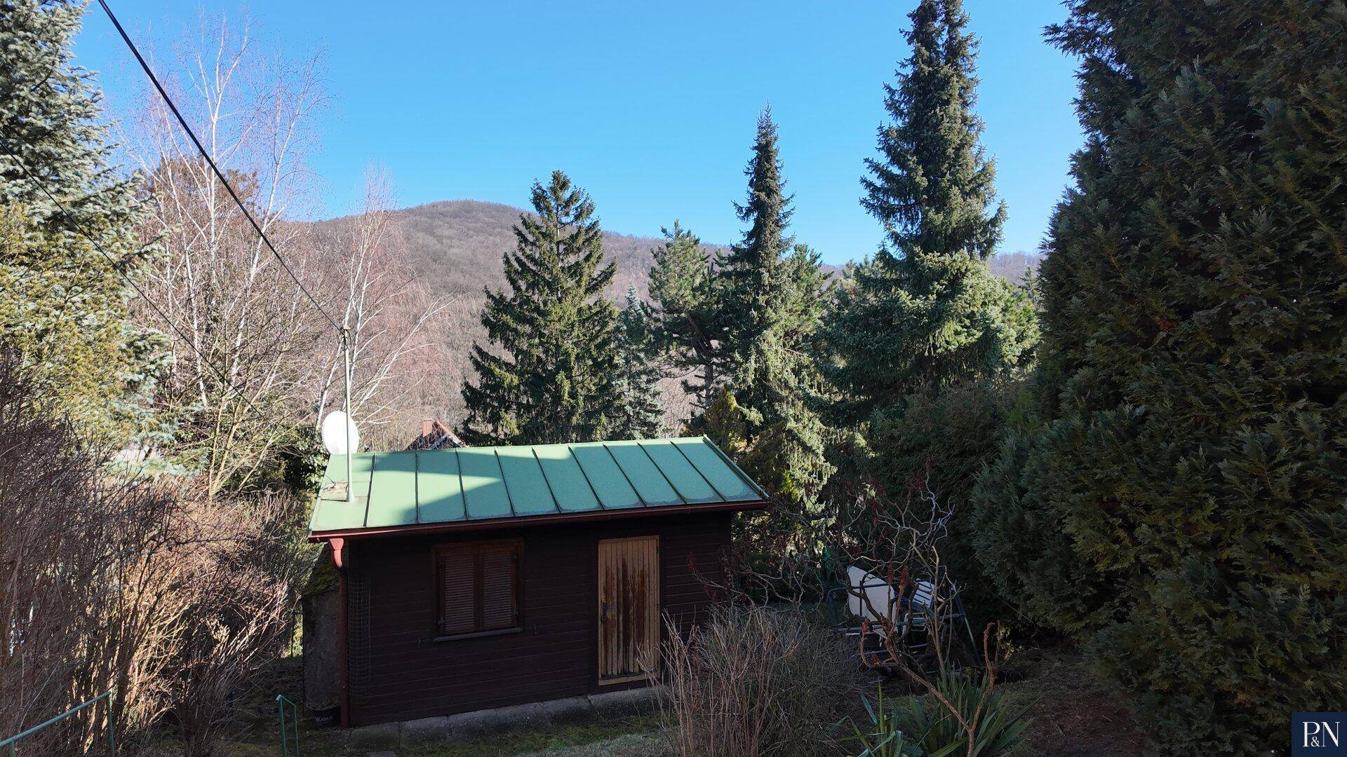 Kleines Holzhaus mit grünem Metalldach, eingebettet in die Natur mit Bergblick.