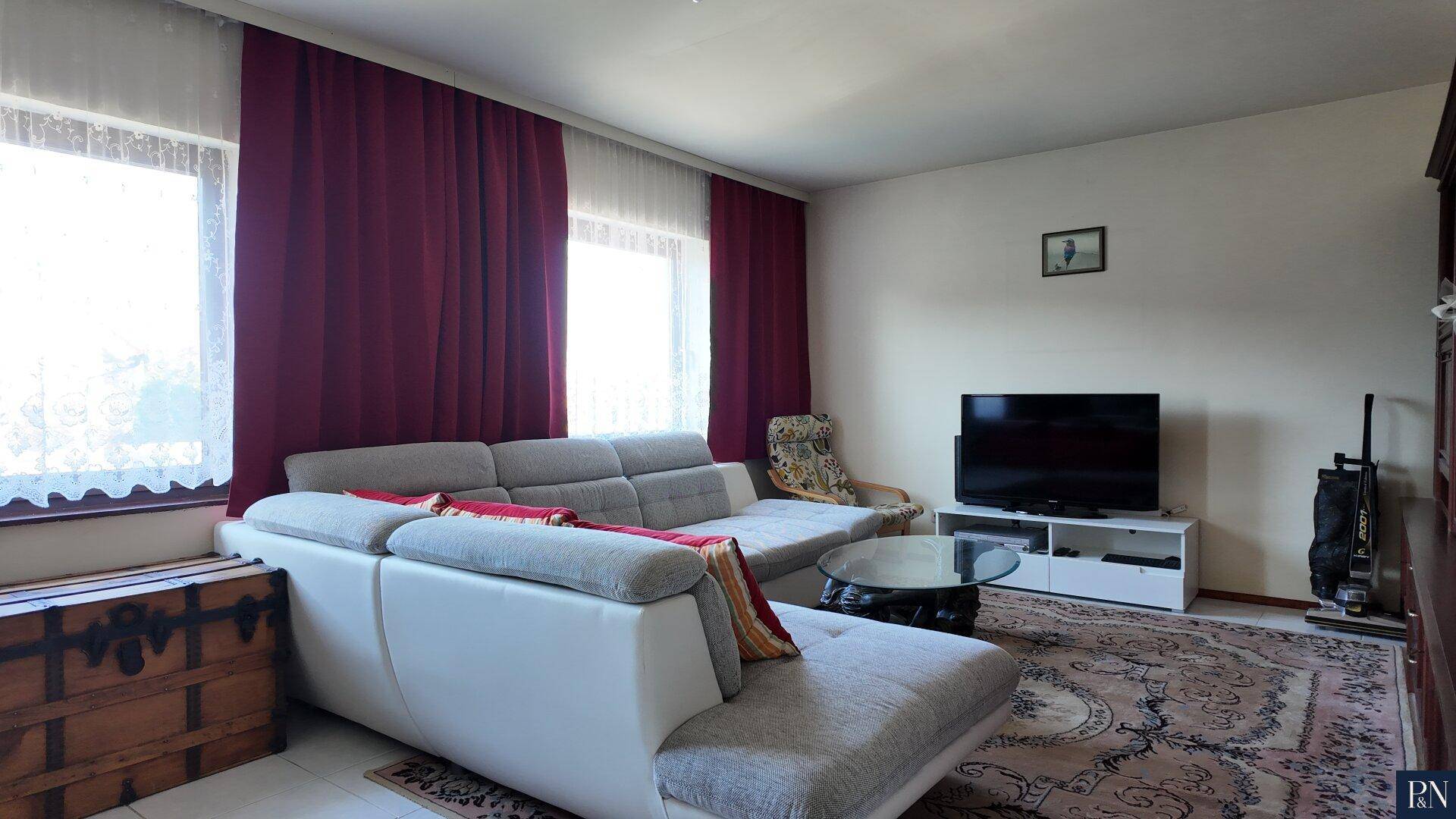 Gemütliches Wohnzimmer mit großem Ecksofa, Teppich und dunklen Vorhängen.