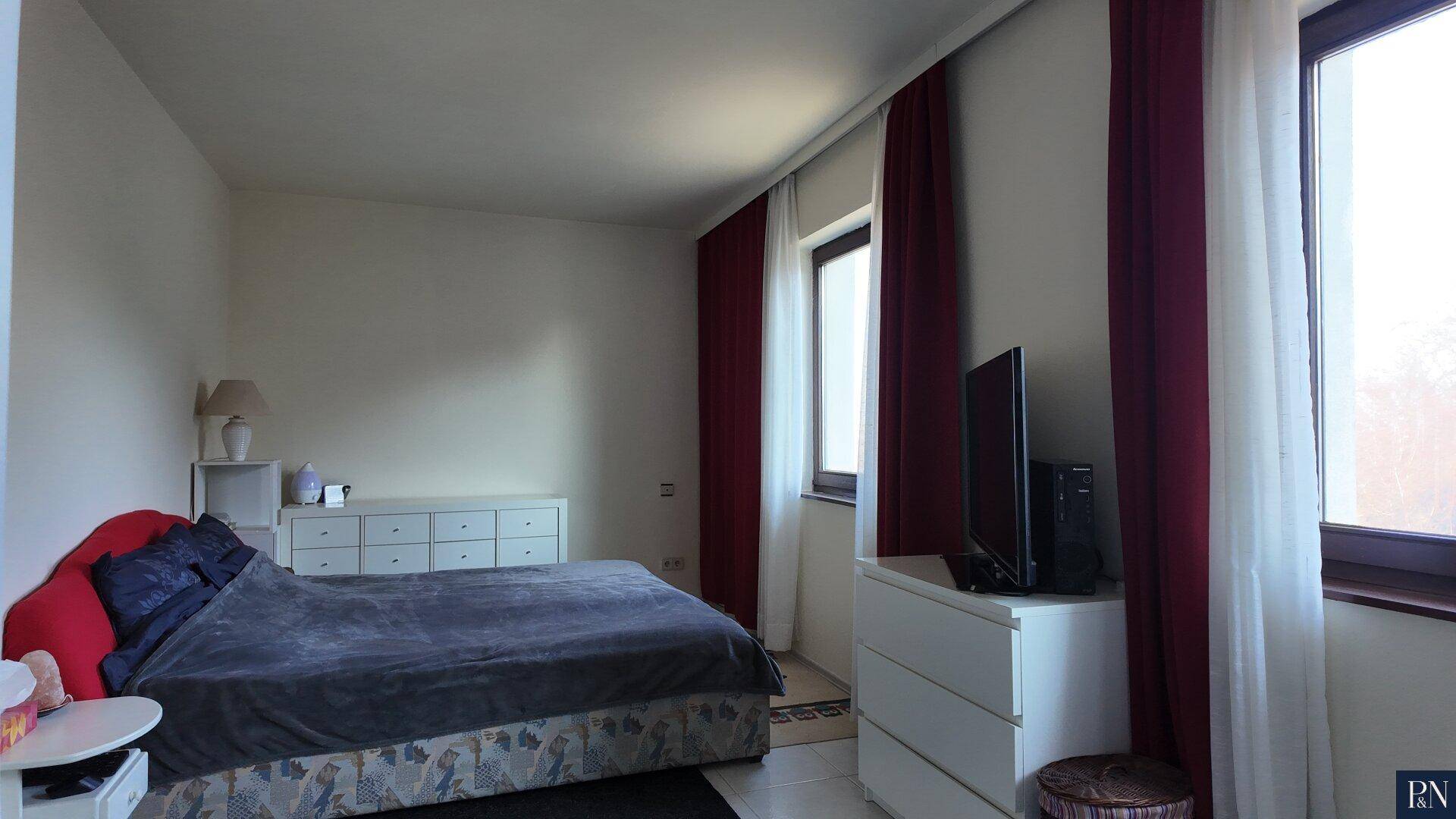Schlafzimmer mit Doppelbett, weißen Kommoden und dunklen Vorhängen an den Fenstern.