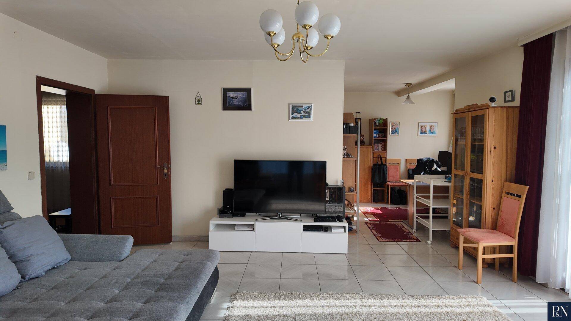 Offener Wohnbereich mit Fliesenboden, Sofa und Blick in einen weiteren Raum.